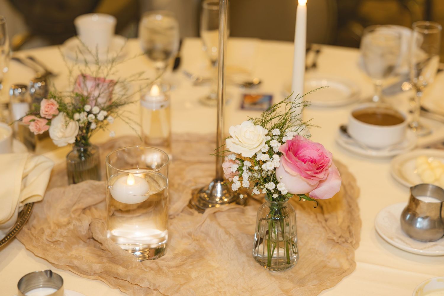 Romantic wedding table centerpiece with pink roses, white flowers, baby\u2019s breath in glass vases and glowing candles.