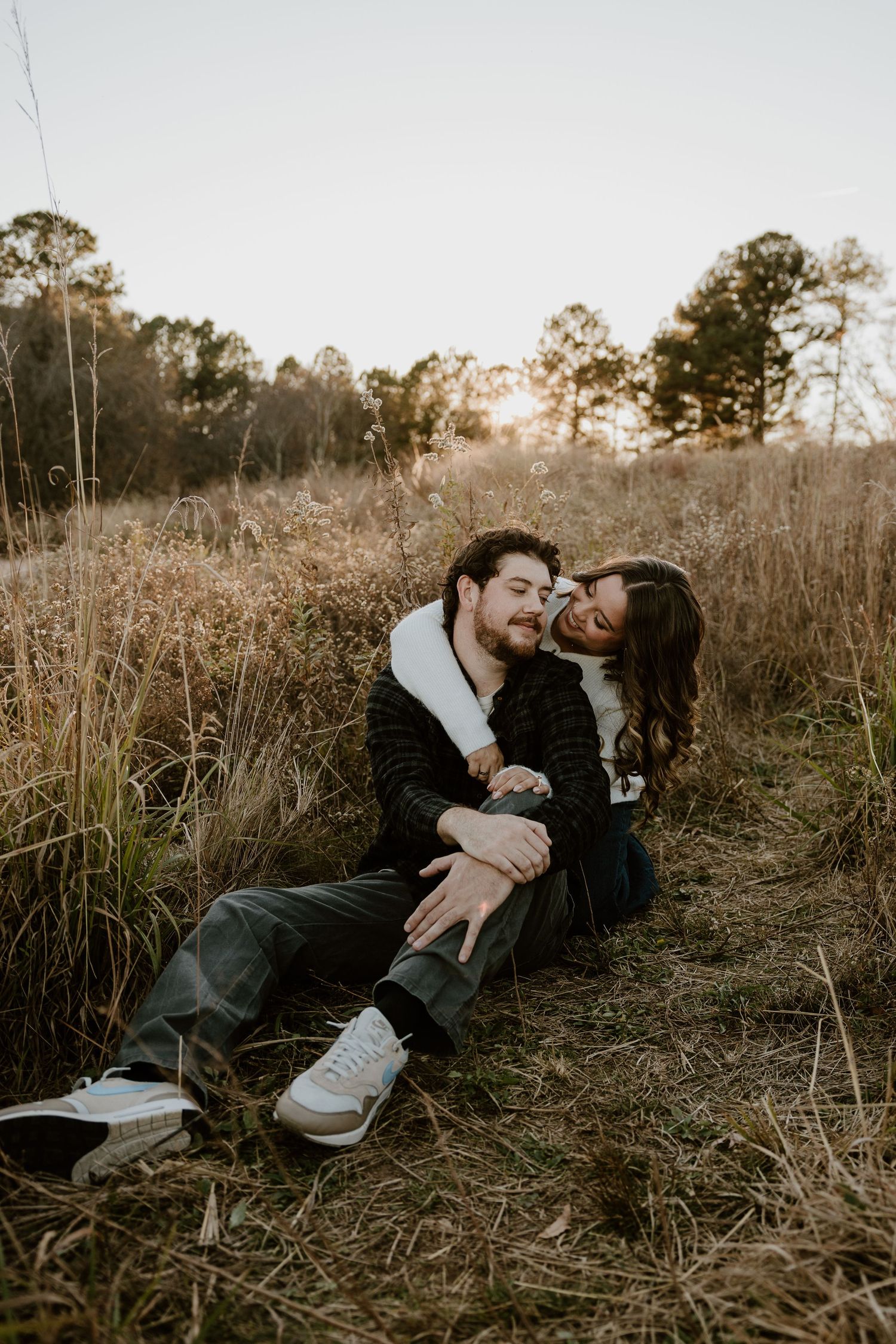 Couple laying in tall grass during golden hour creating intimate candid moments.