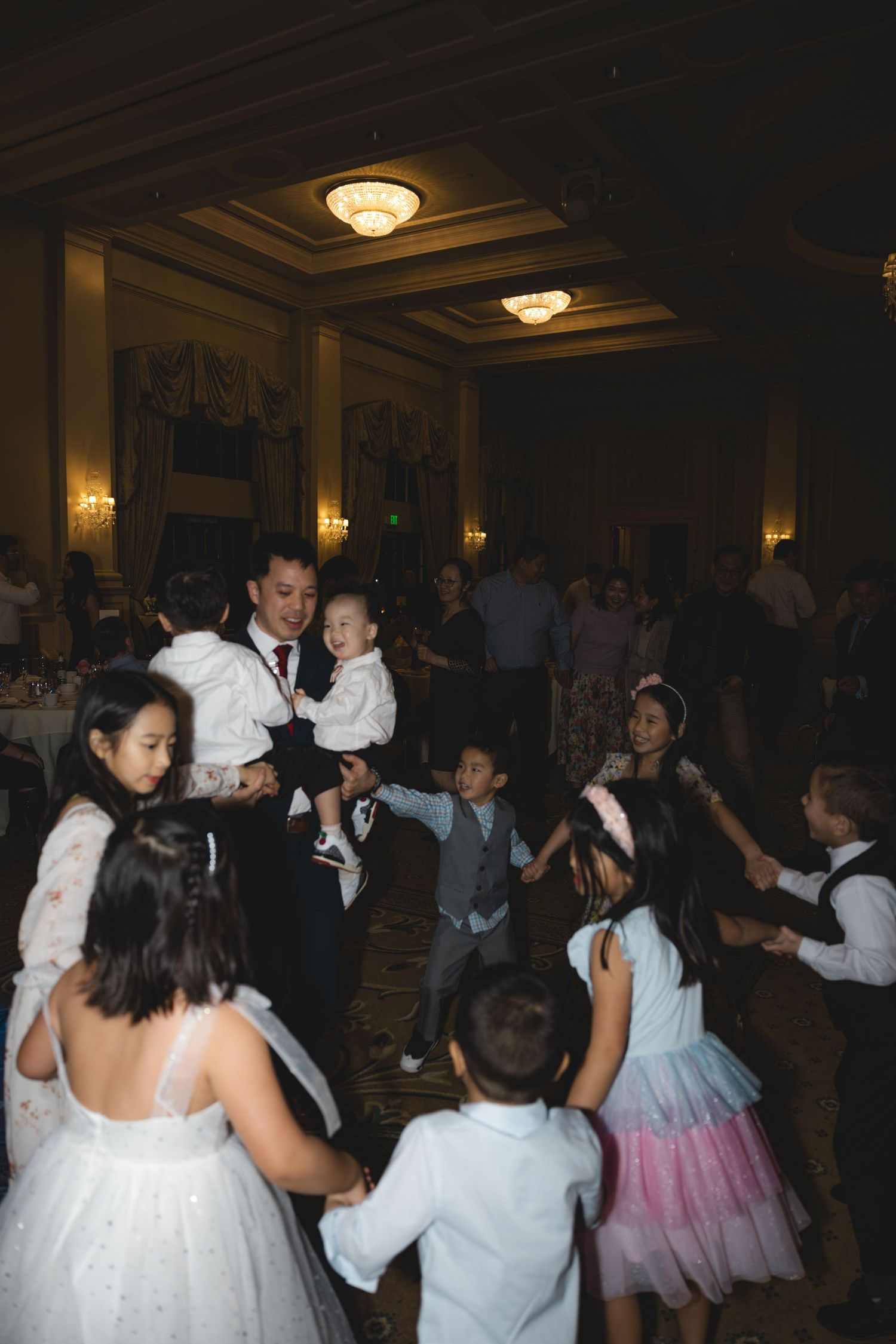 Groom dancing with children on the wedding reception dance floor in ballroom.