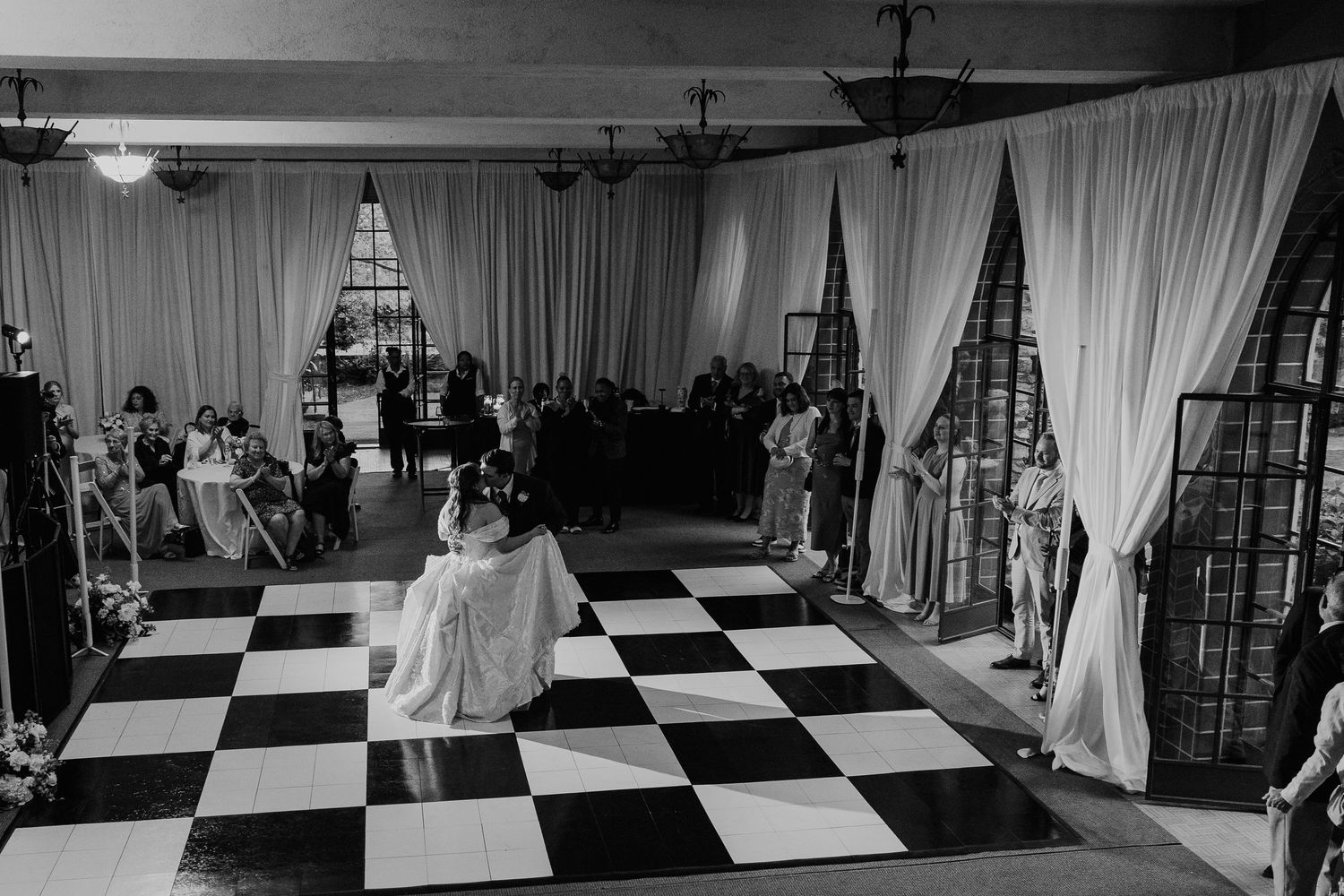 Couple shares first dance on checkered floor at elegant wedding reception in black and white photo.