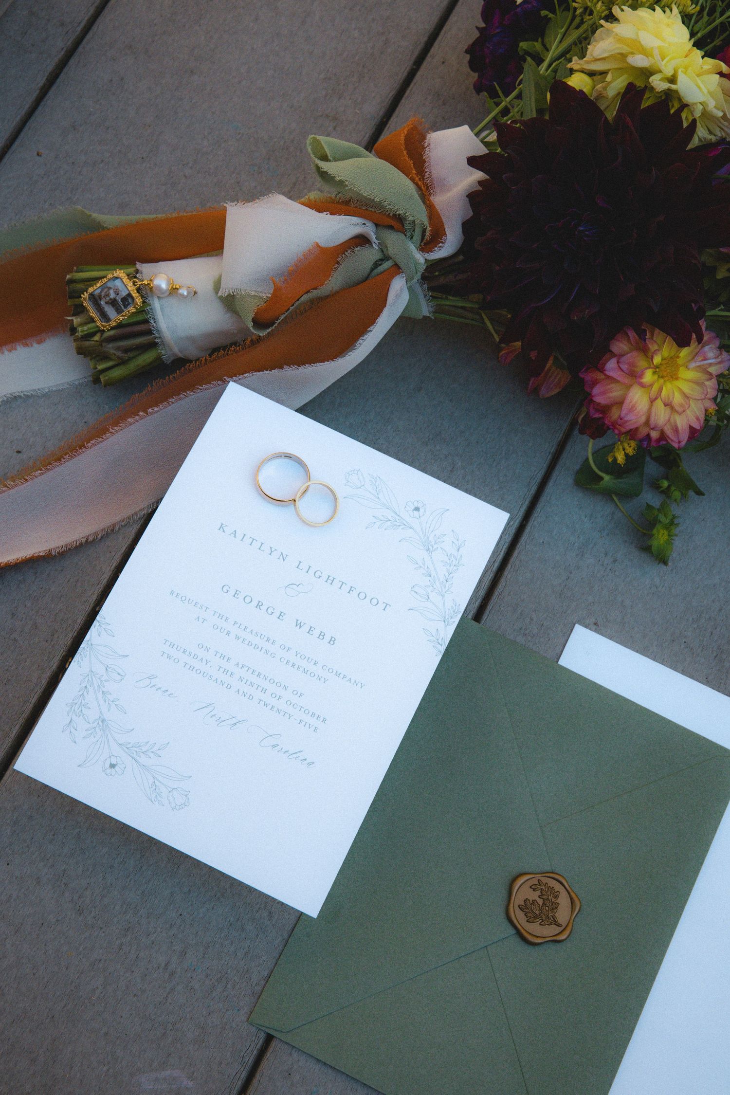 An image showing a wedding invitation, wedding rings, and a bouquet of flowers on a wooden surface.