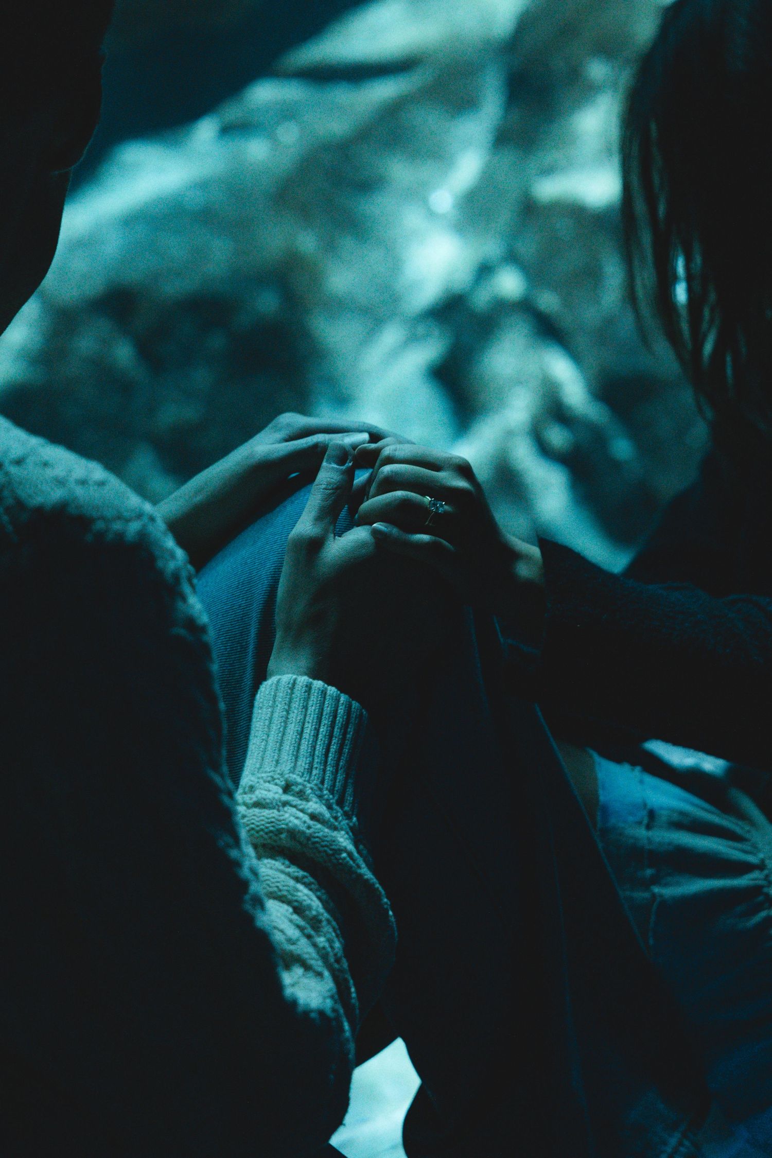 Close-up of hands wearing knit sweaters in moody blue-tinted lighting.