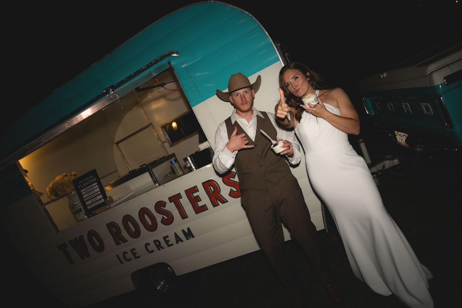Bride and groom posing in front of Two Roosters Ice Cream food truck at night.