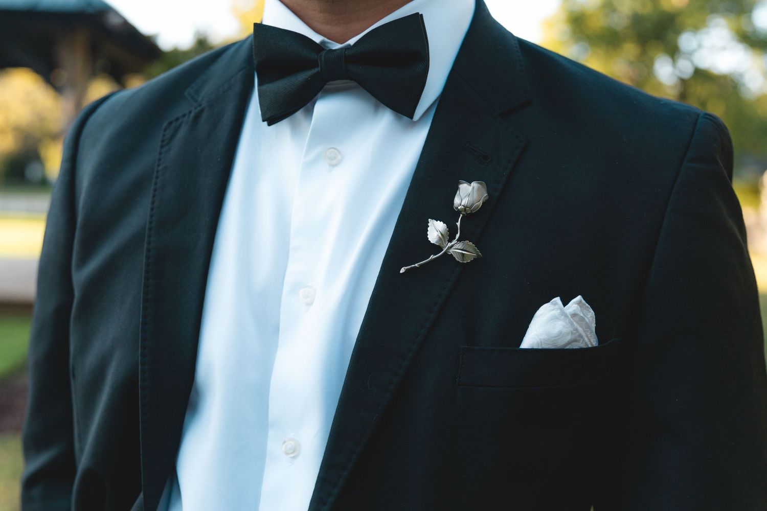 Groom in a dark suit jacket with black bow tie, white dress shirt, silver rose boutonniere and white pocket square.