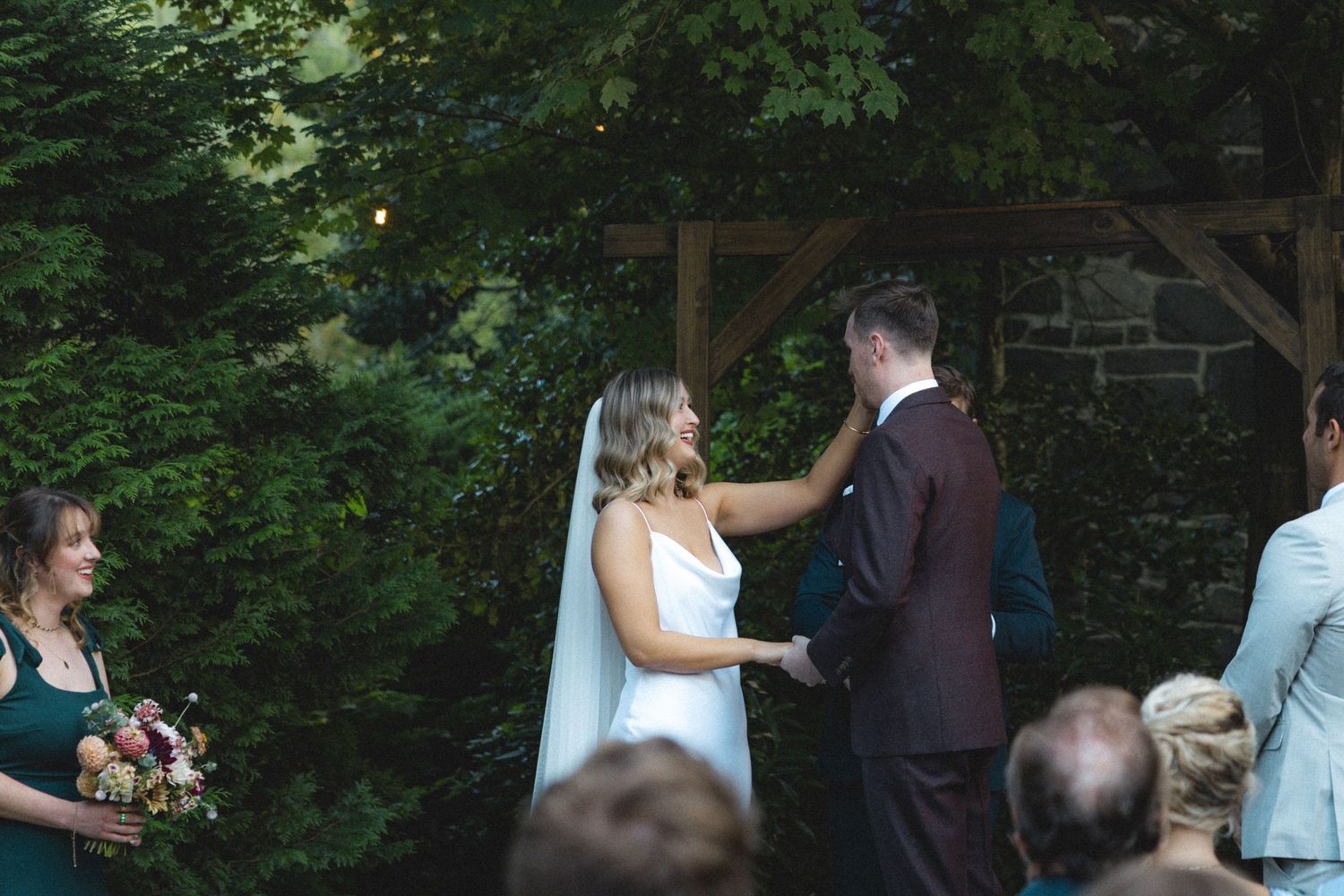 Bride and groom exchange vows at outdoor wedding ceremony surrounded by lush greenery and stone architecture.