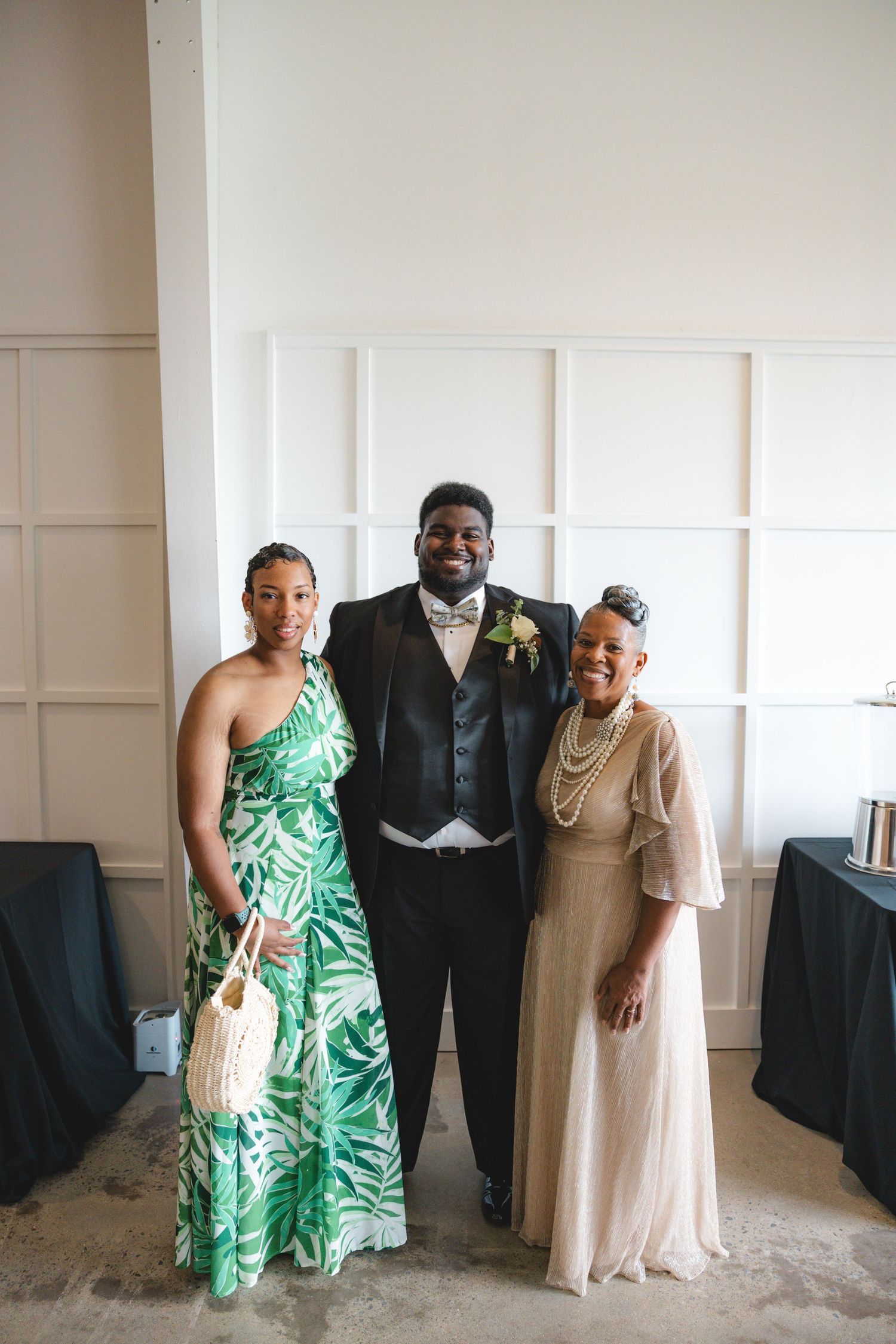 A groom in a tuxedo poses with two women in elegant attire at a wedding reception venue.