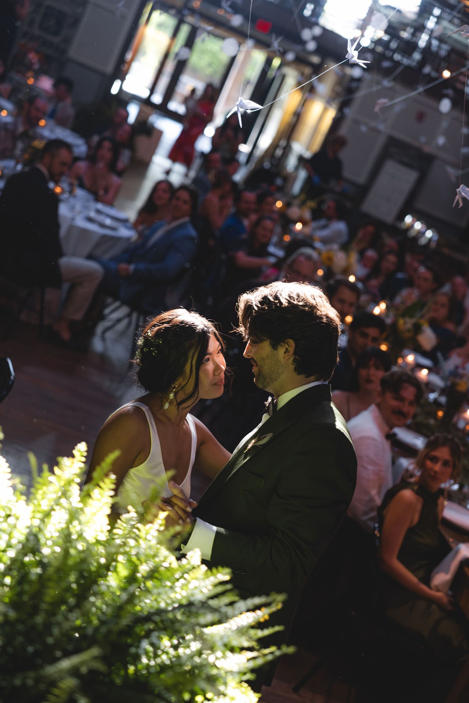 Bride and groom share their first dance at a romantic indoor wedding reception with guests watching in the background.