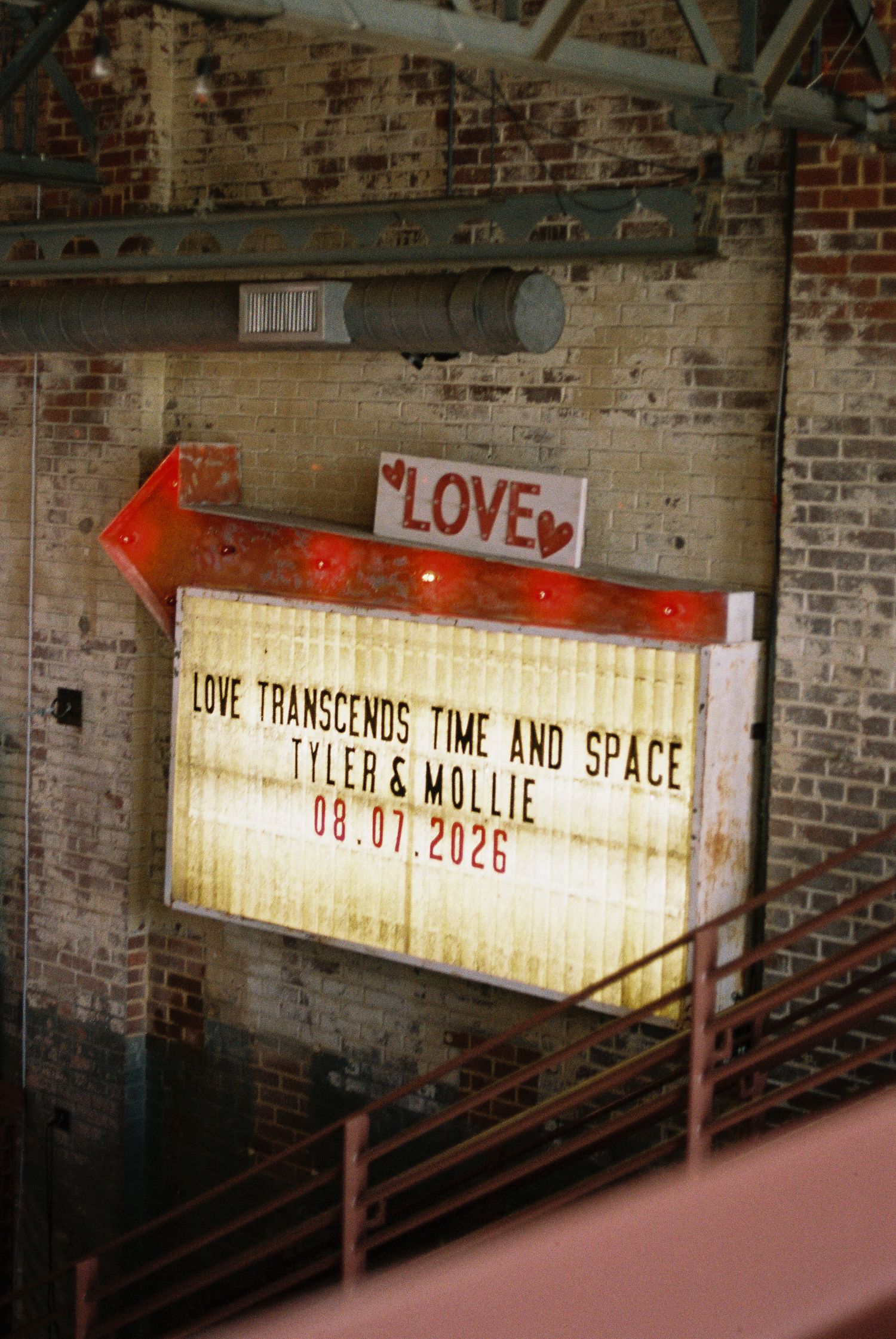 Vintage marquee sign reading Love Transcends Time and Space, Tyler & Mollie 08.07.2026 in rustic brick venue.