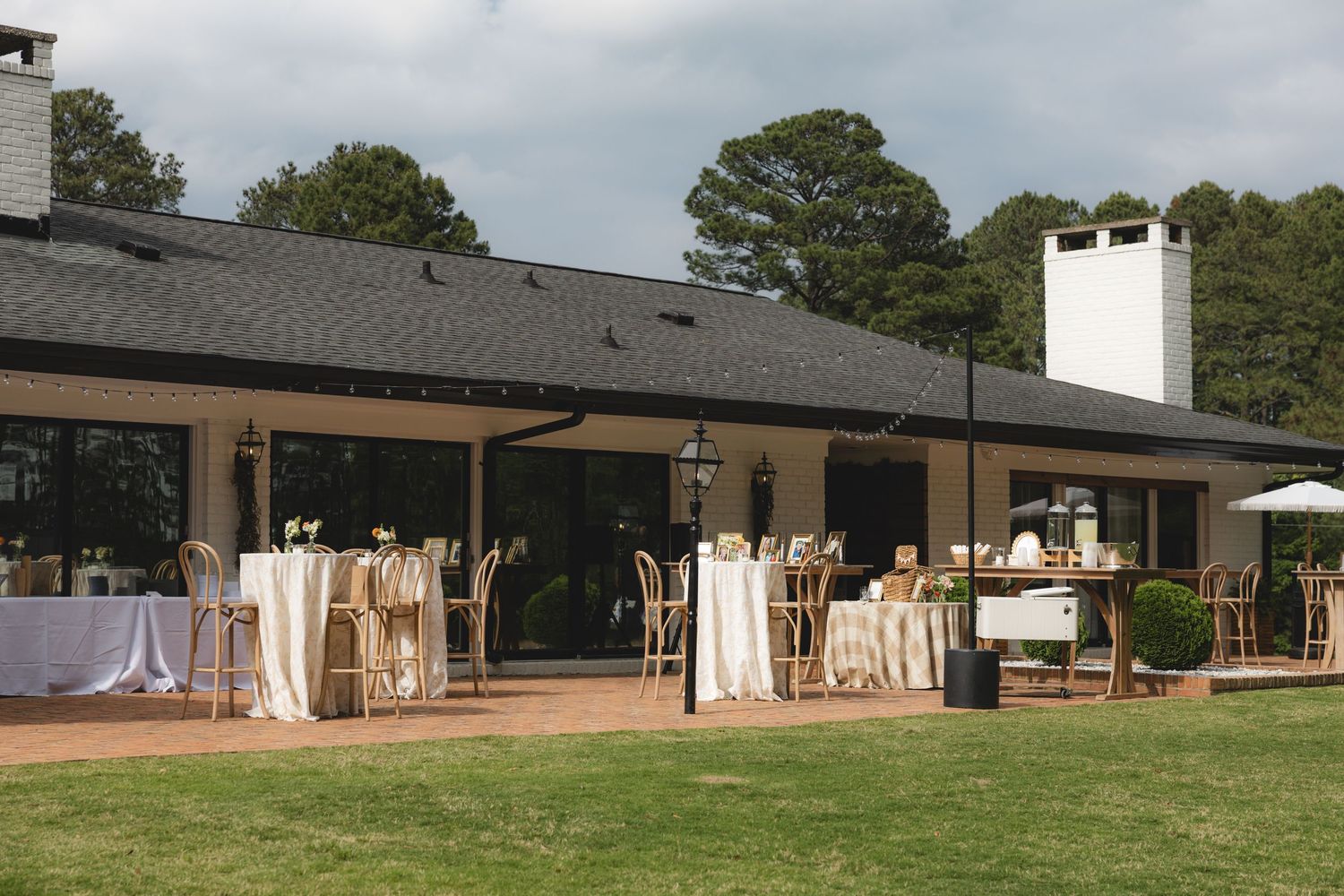 Elegant outdoor wedding reception setup with white draped tables on a patio beside a charming venue building.