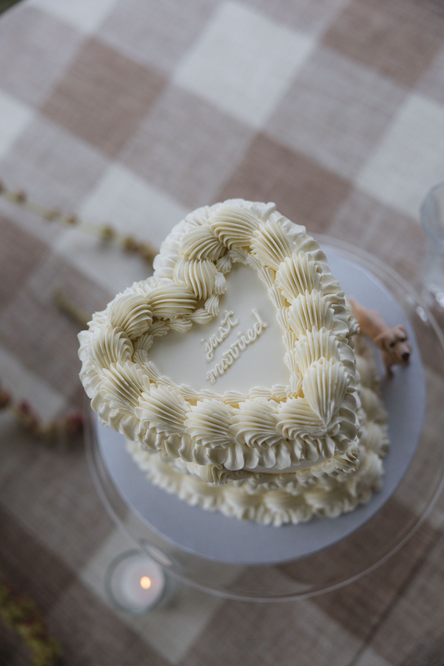 Heart-shaped white wedding cake with ruffled buttercream frosting and just married inscription on glass stand.