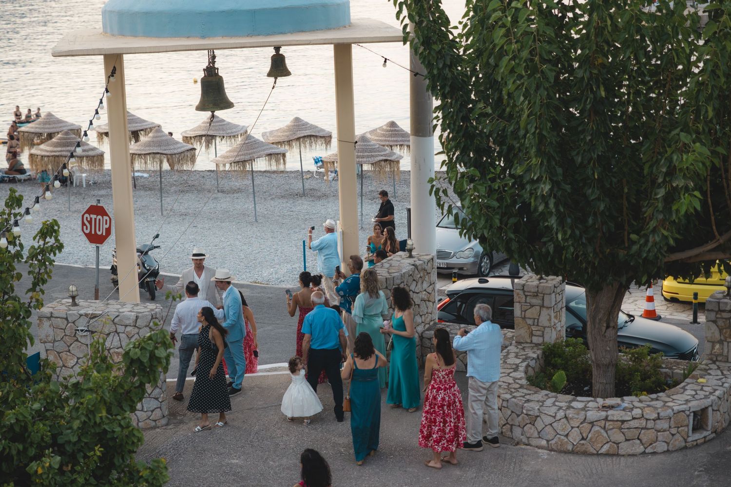 Guests gather near a seaside bell tower during an outdoor wedding celebration in a Mediterranean coastal town.