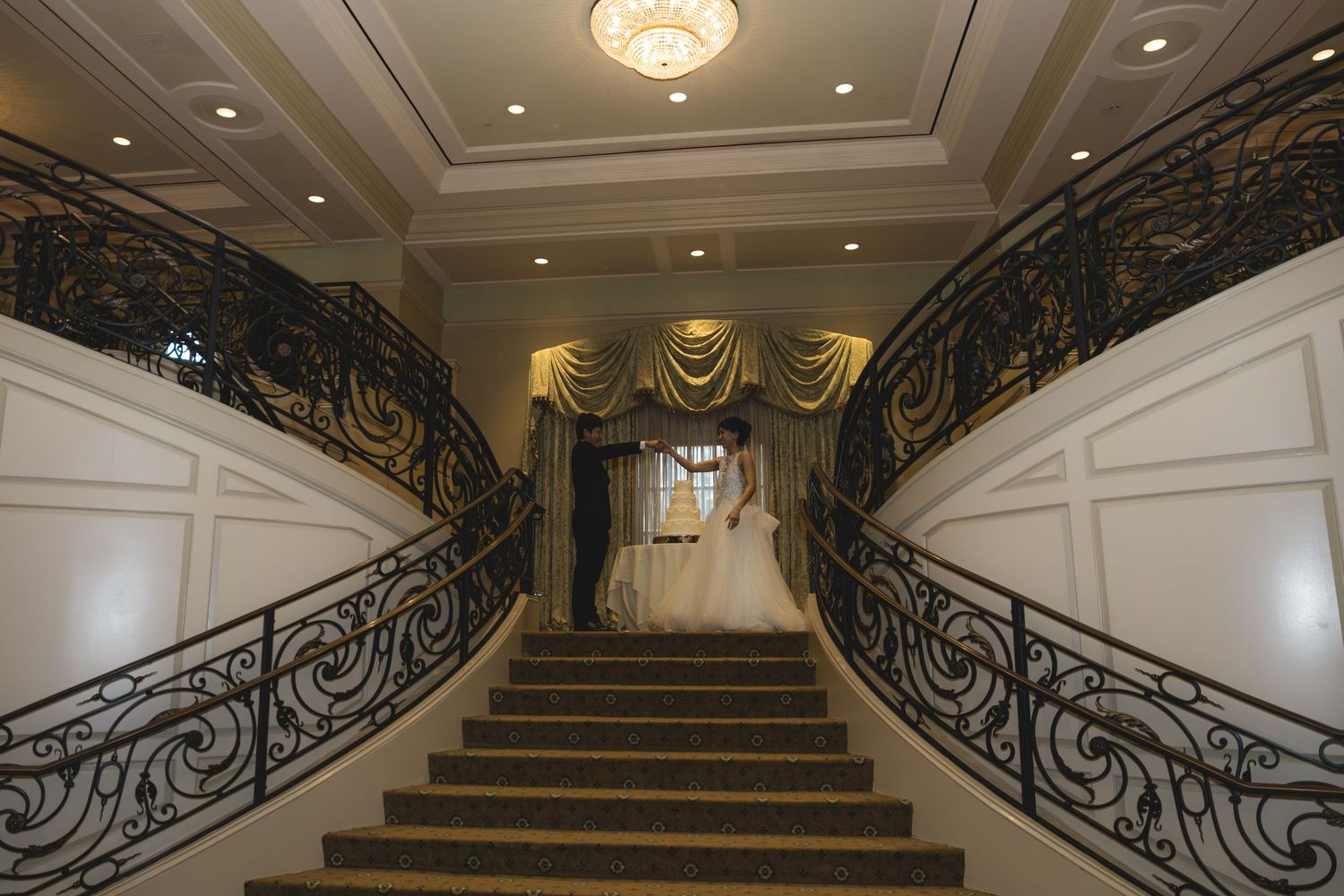 Bride ascending grand staircase with ornate black railings in luxurious wedding venue.