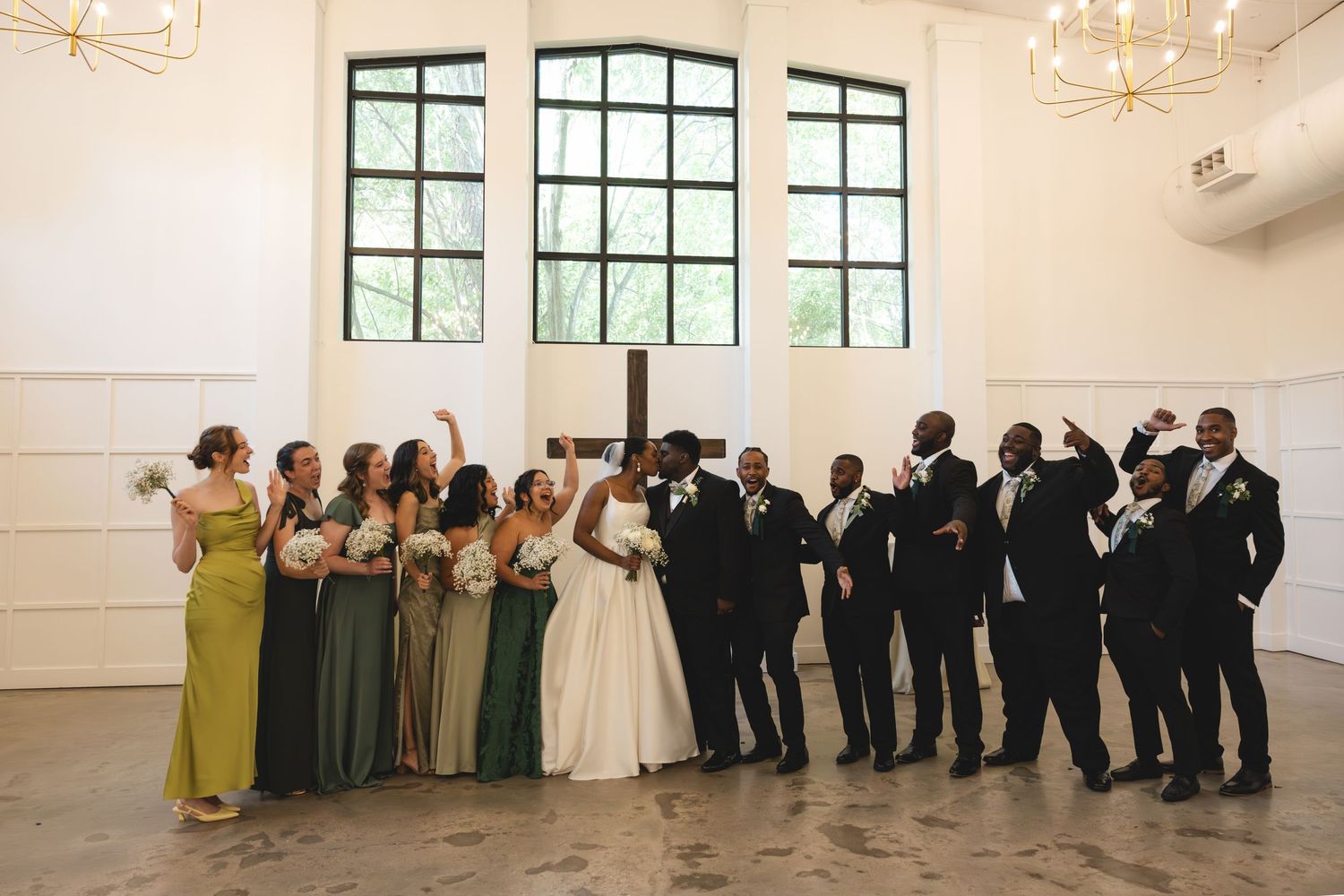 Wedding party celebrates together in bright venue with bridesmaids in green gowns and groomsmen in black suits.