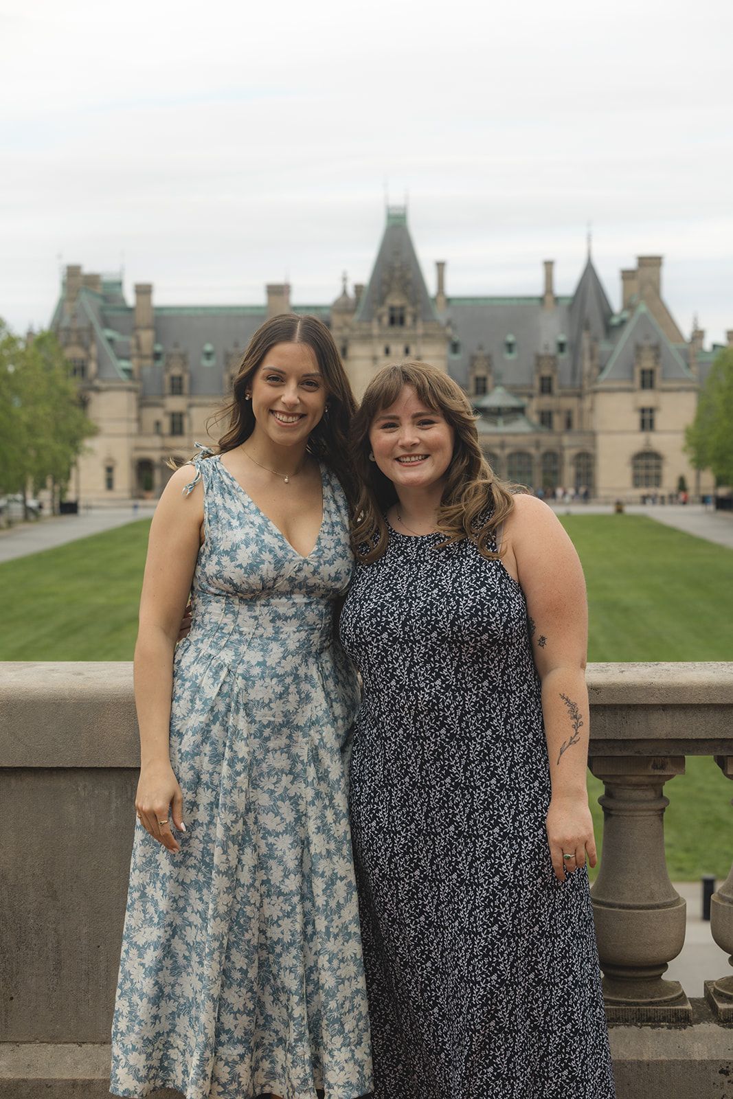 Two women in summer dresses smiling together in front of the Biltmore Estate in Asheville, NC.