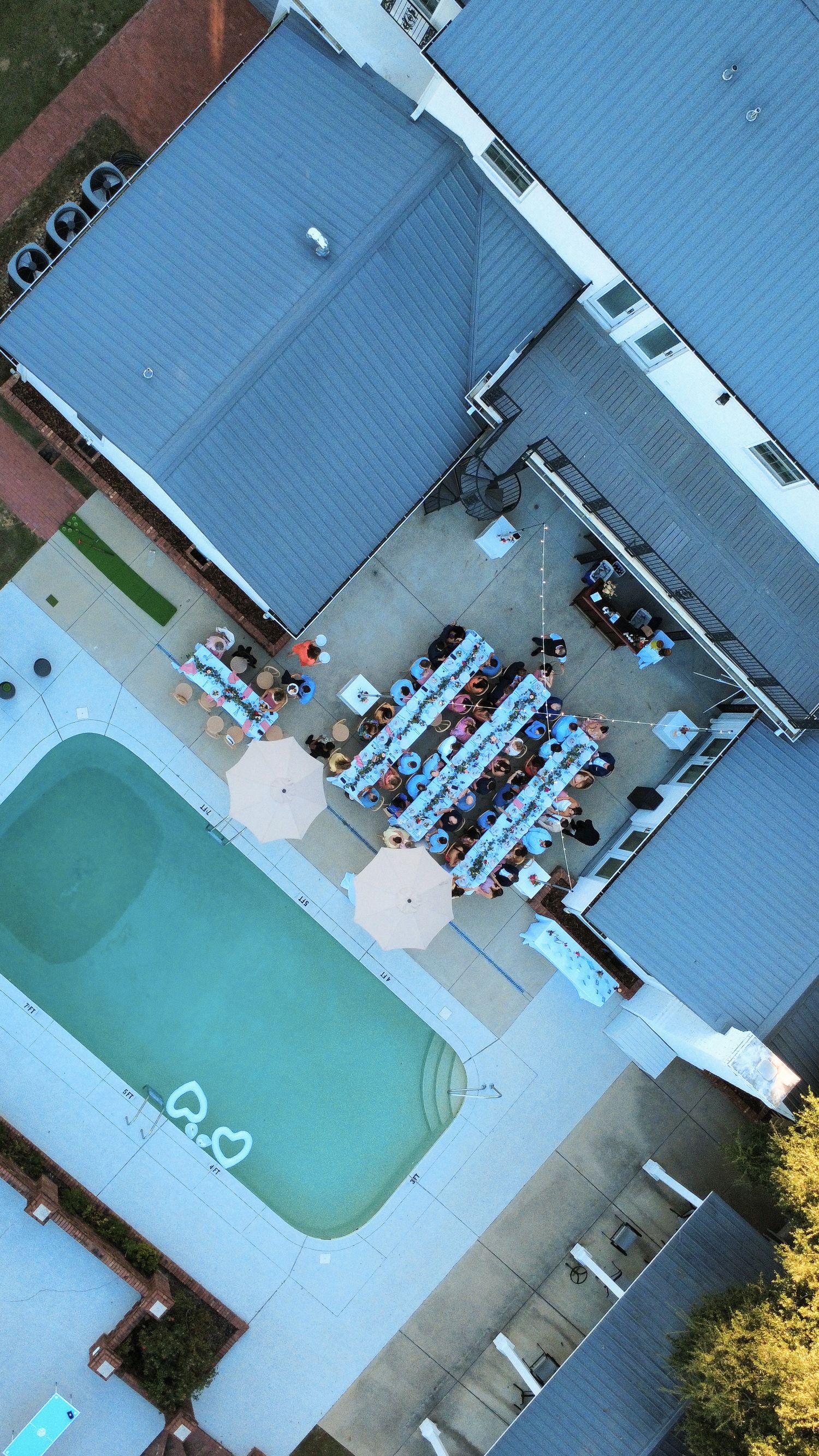 Aerial drone view of an outdoor wedding reception with decorated tables beside a swimming pool at a private estate.