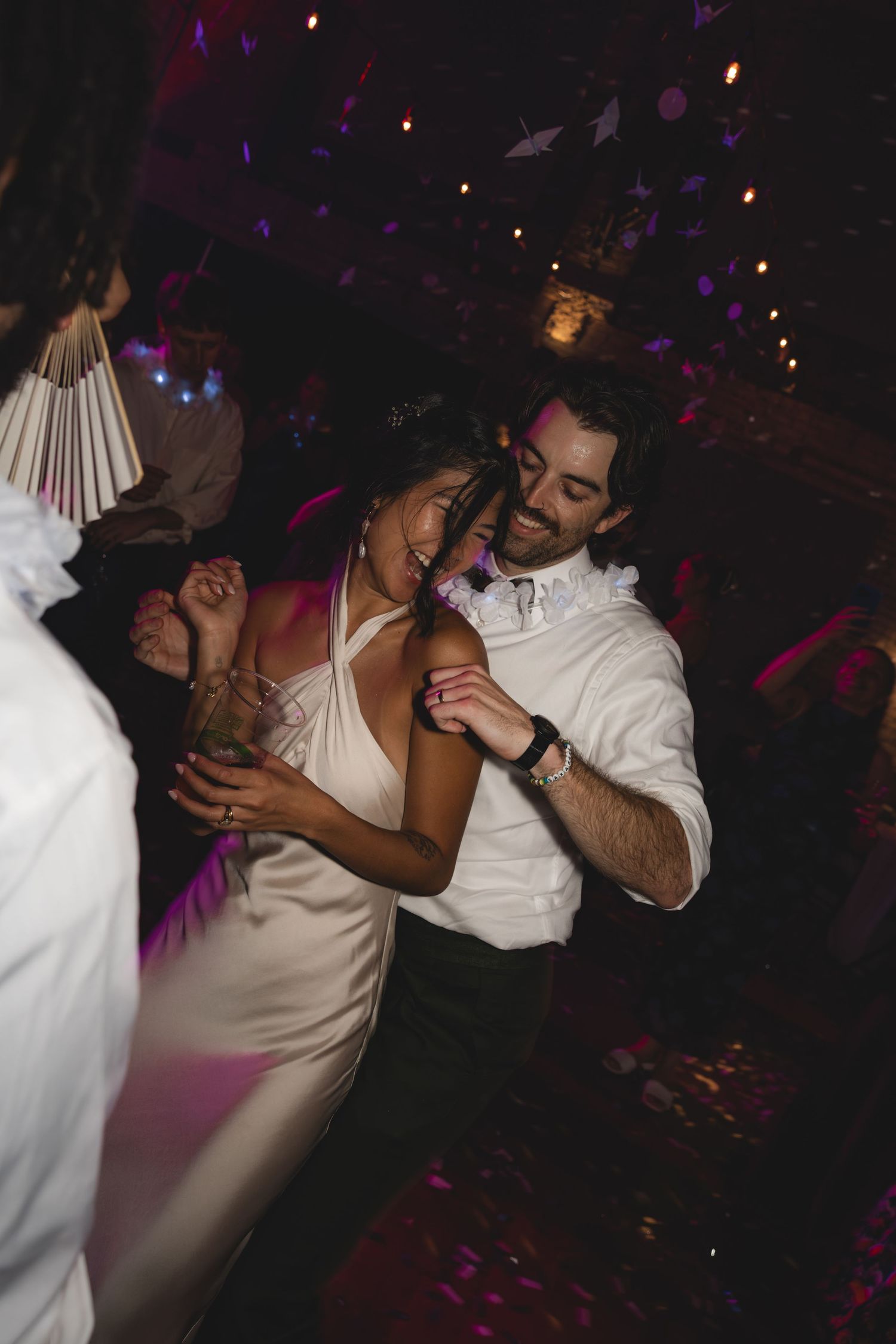 Bride and groom share a joyful dance together at their wedding reception under warm purple lights.