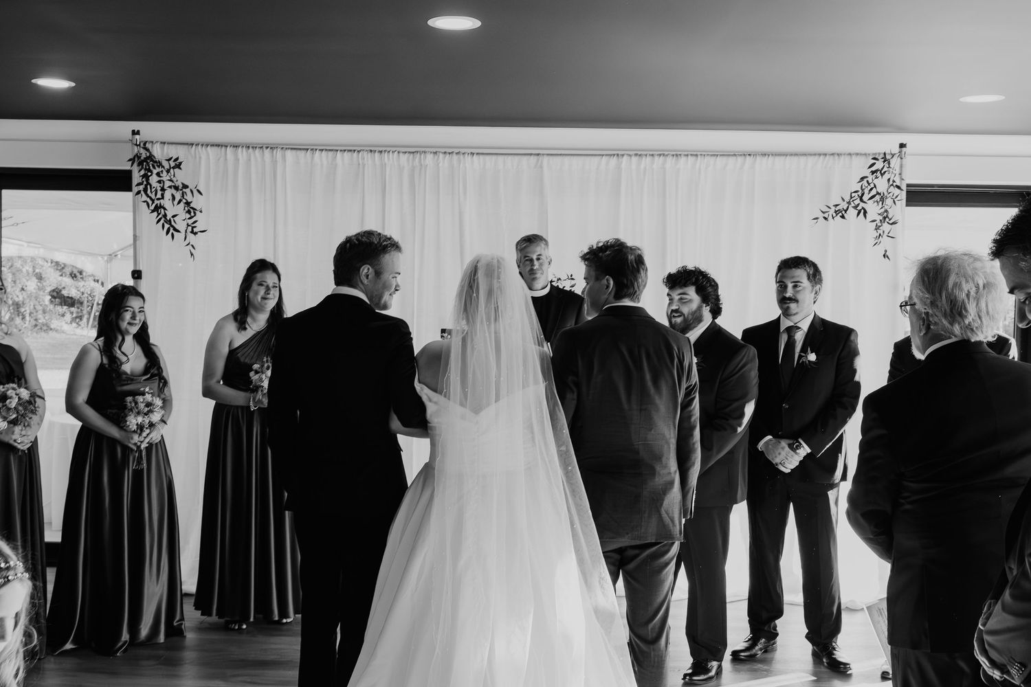 Wedding ceremony in progress with bridal party and guests gathered in an indoor venue.