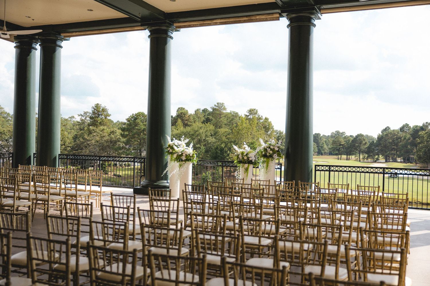 Elegant outdoor wedding venue with gold chiavari chairs, white floral arrangements, and scenic golf course views.