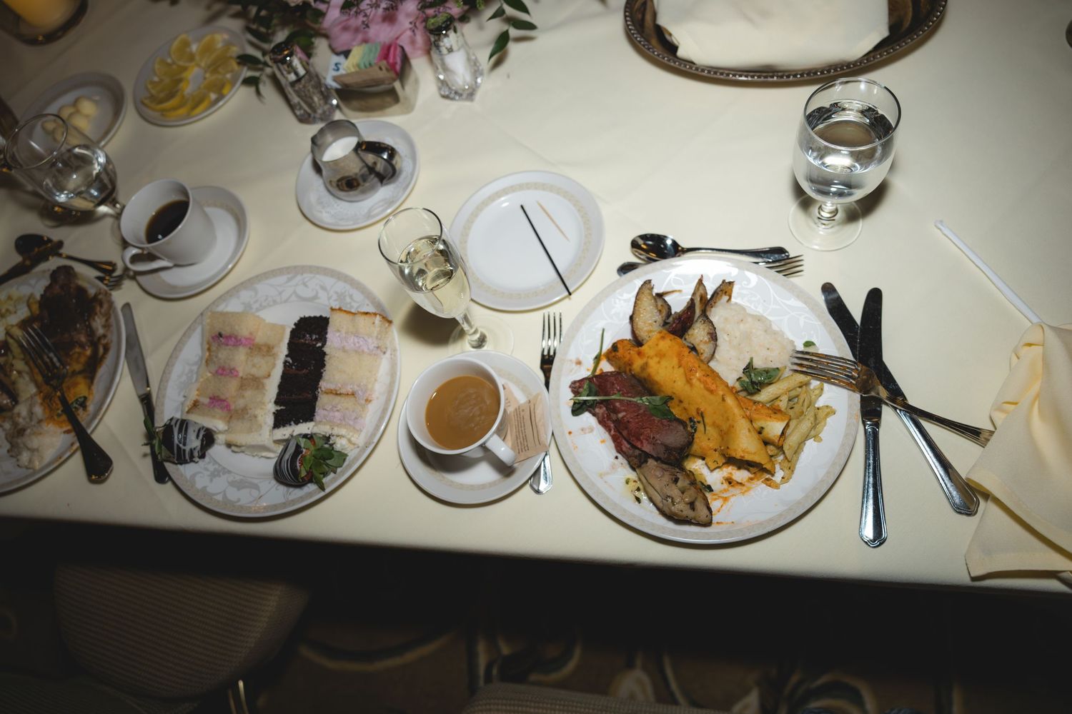 Overhead view of elegant wedding reception dinner plates with lobster and gourmet dishes on white tablecloth.