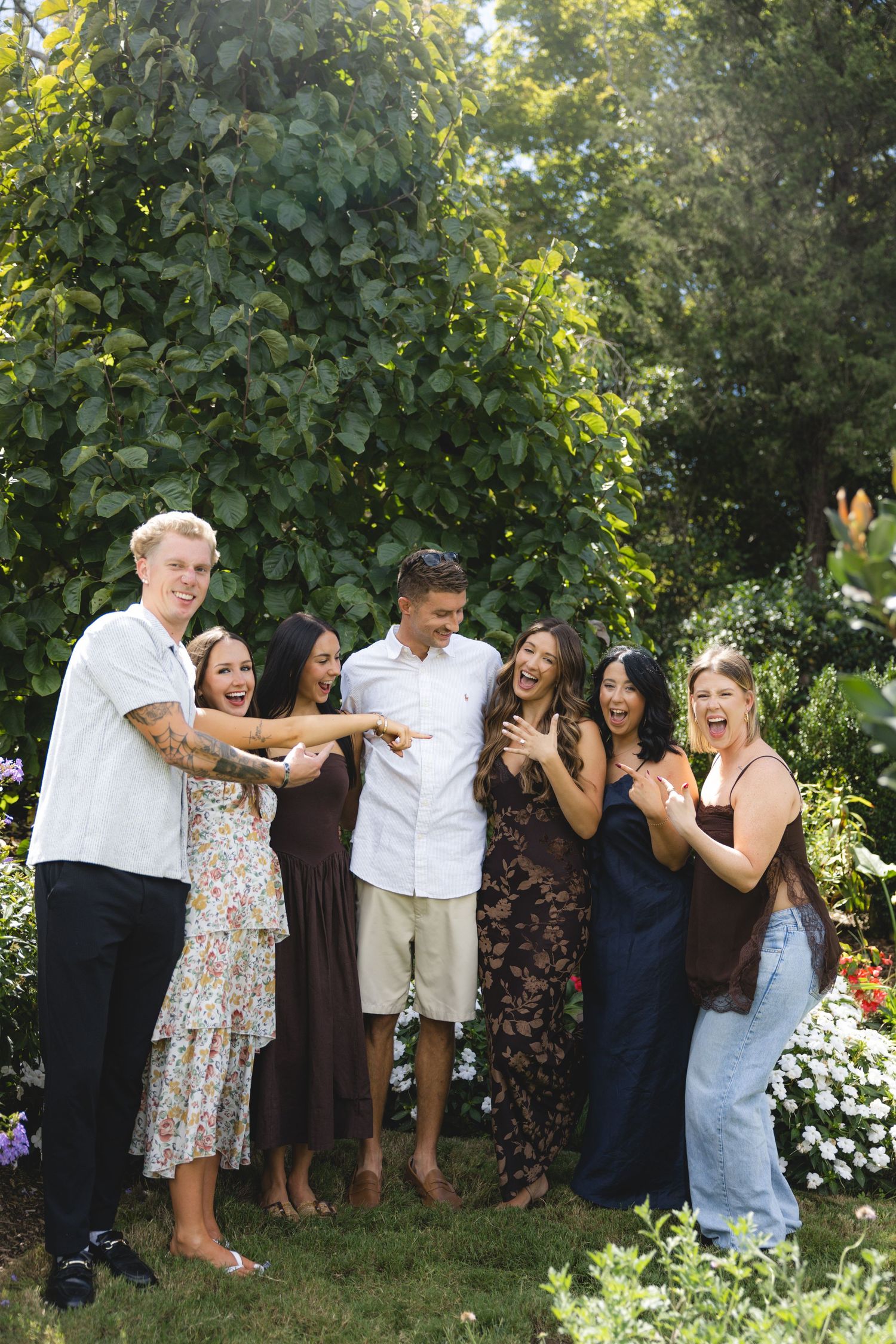 A joyful group of six friends laughing and celebrating outdoors in a lush garden setting.