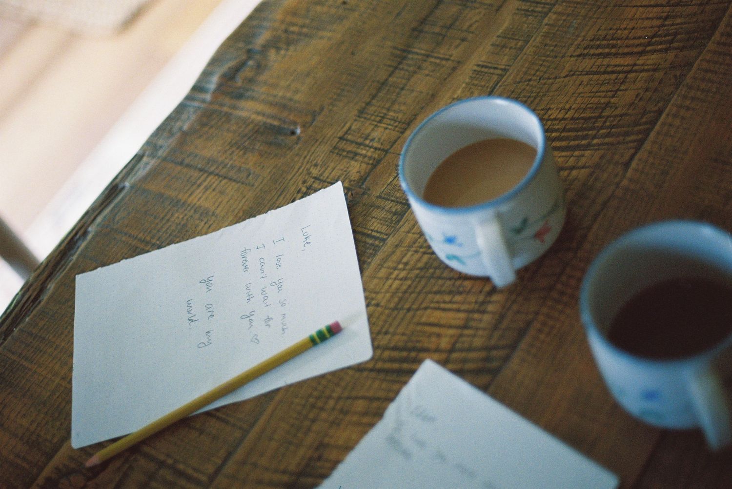 Two mugs of coffee and a pencil on handwritten notes spread across a rustic wooden table.