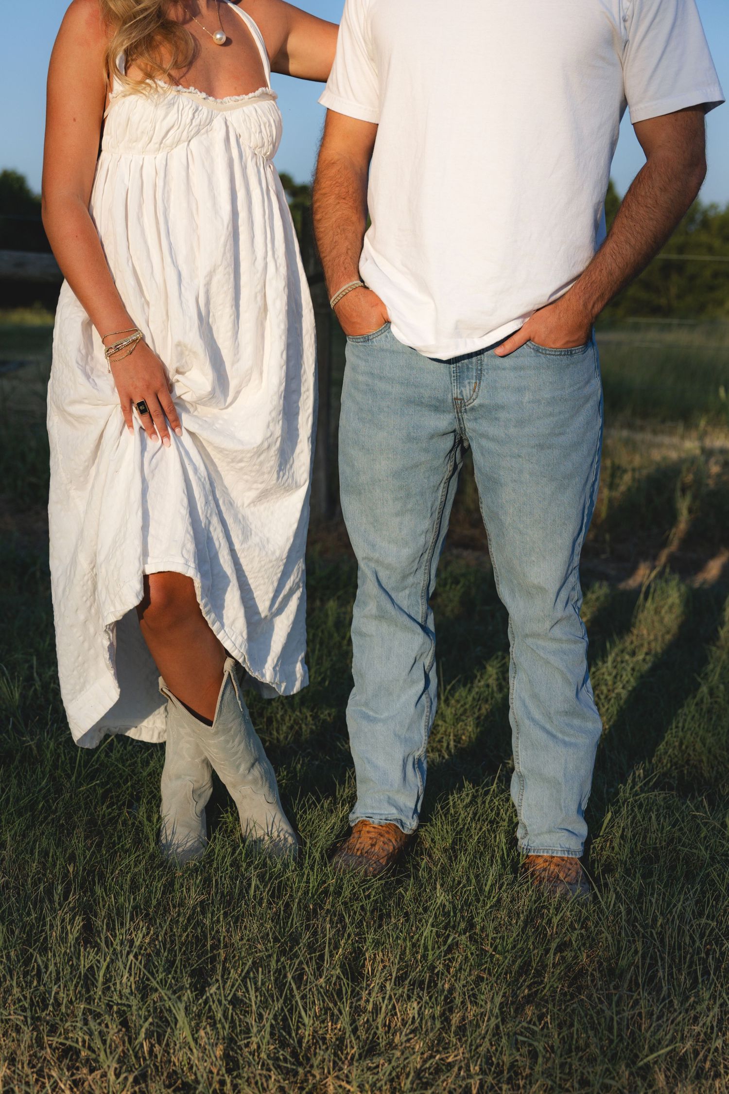 Couple standing in a field, woman in white dress and cowboy boots, man in jeans and white t-shirt.