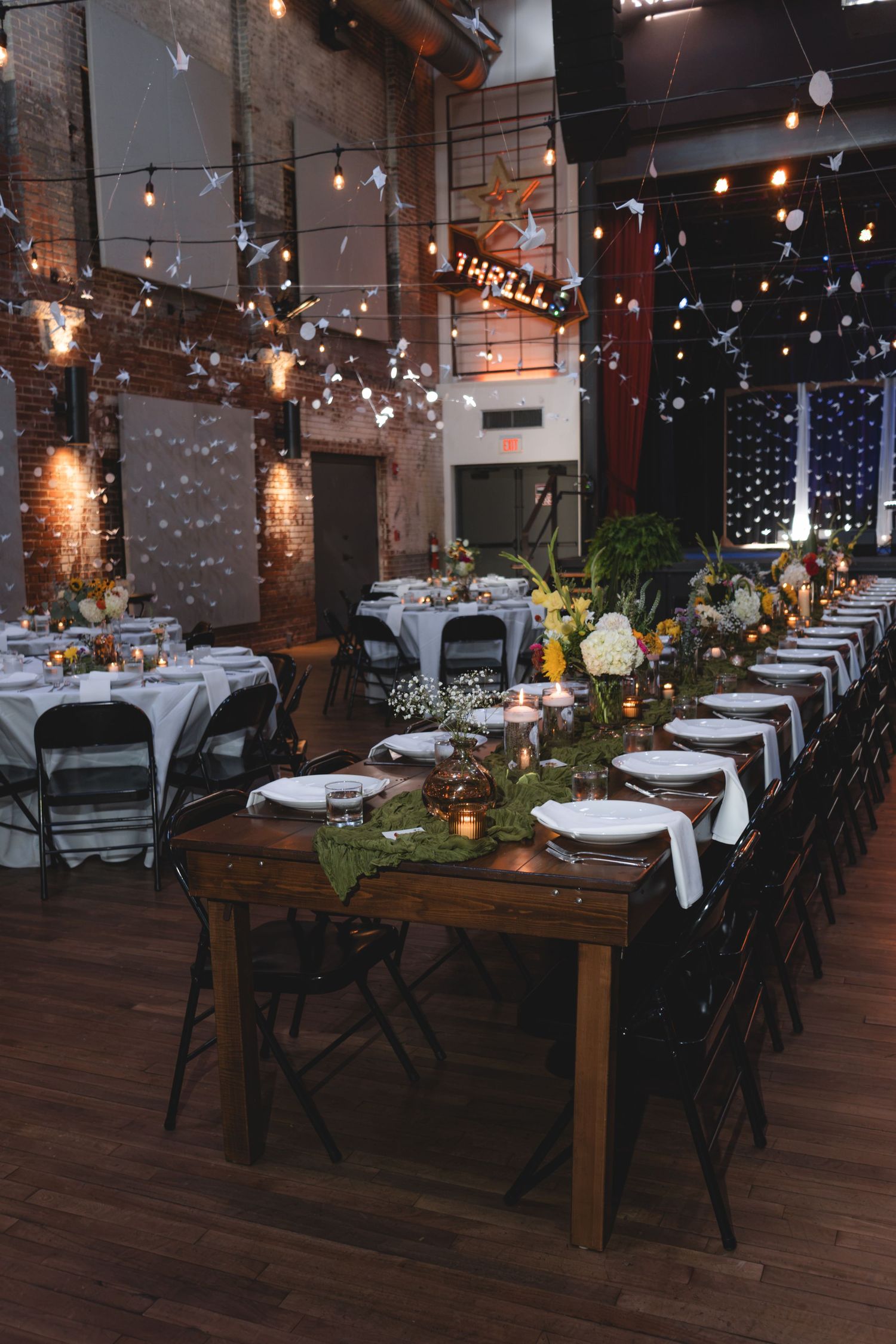 Elegant wedding reception venue with string lights, floral centerpieces, and rustic wooden tables set for dining.