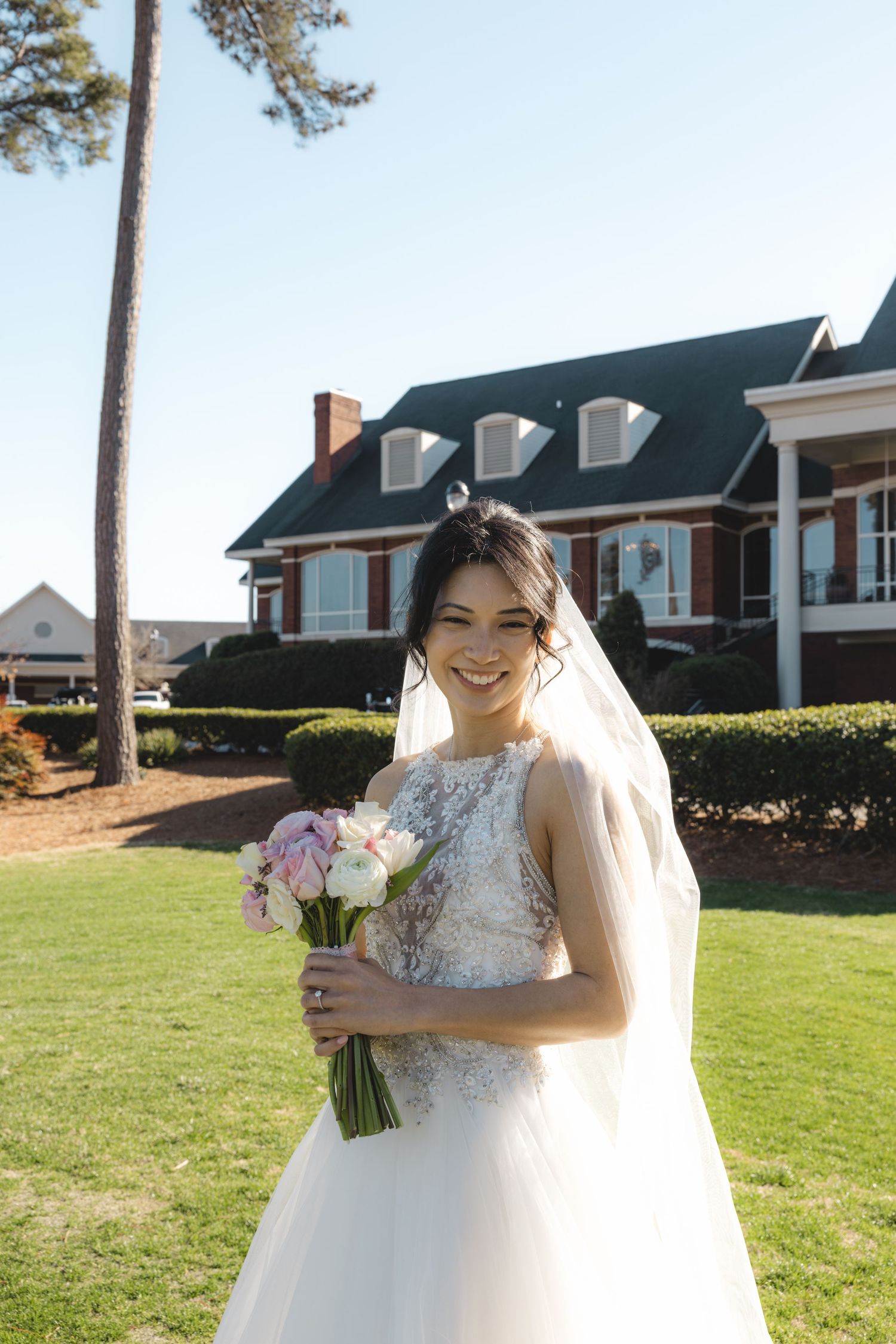 Radiant bride in lace wedding gown holding pink and white bouquet outdoors at elegant venue.