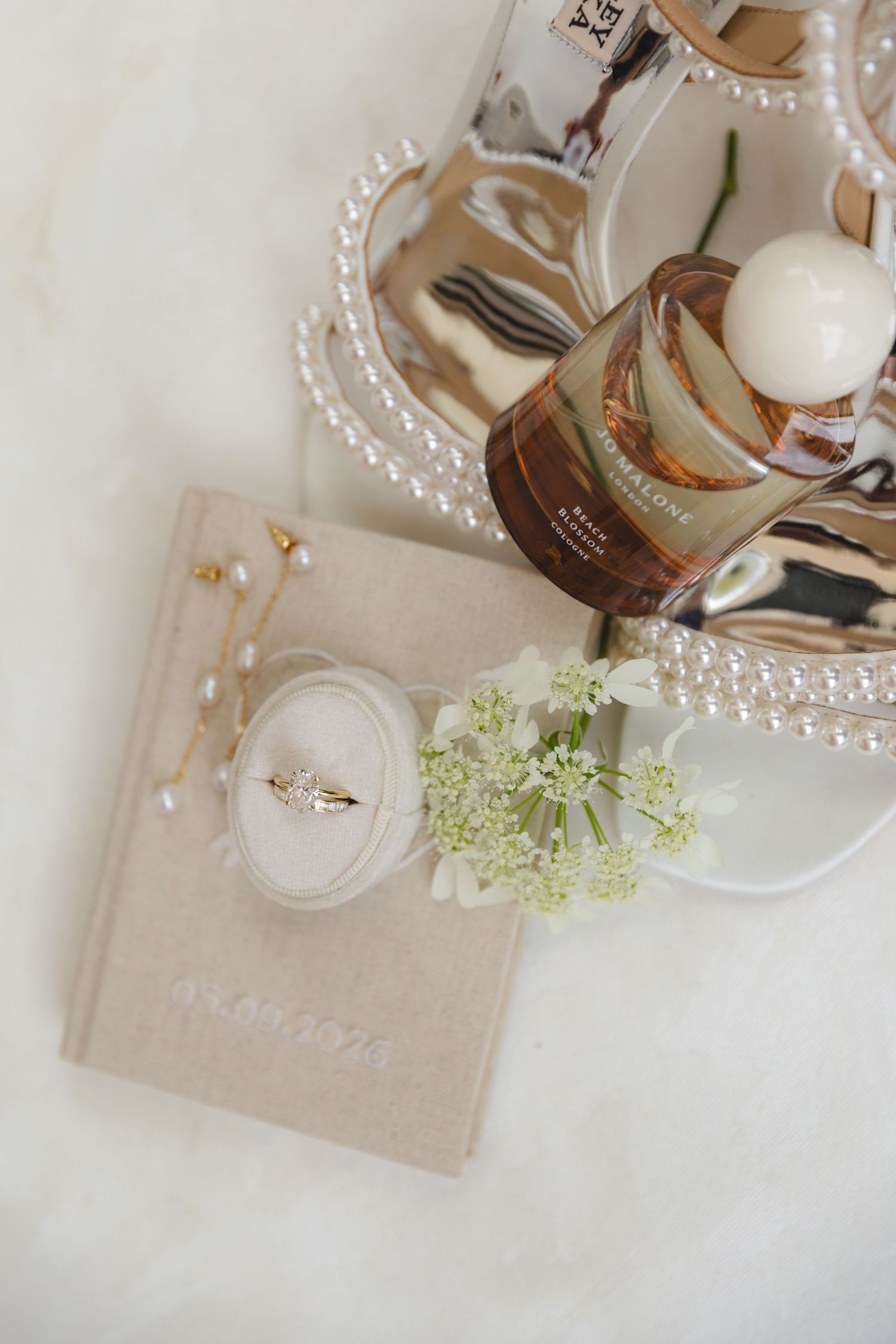 Elegant bridal flat lay with engagement ring, pearl necklace, perfume, and floral details on white fur.