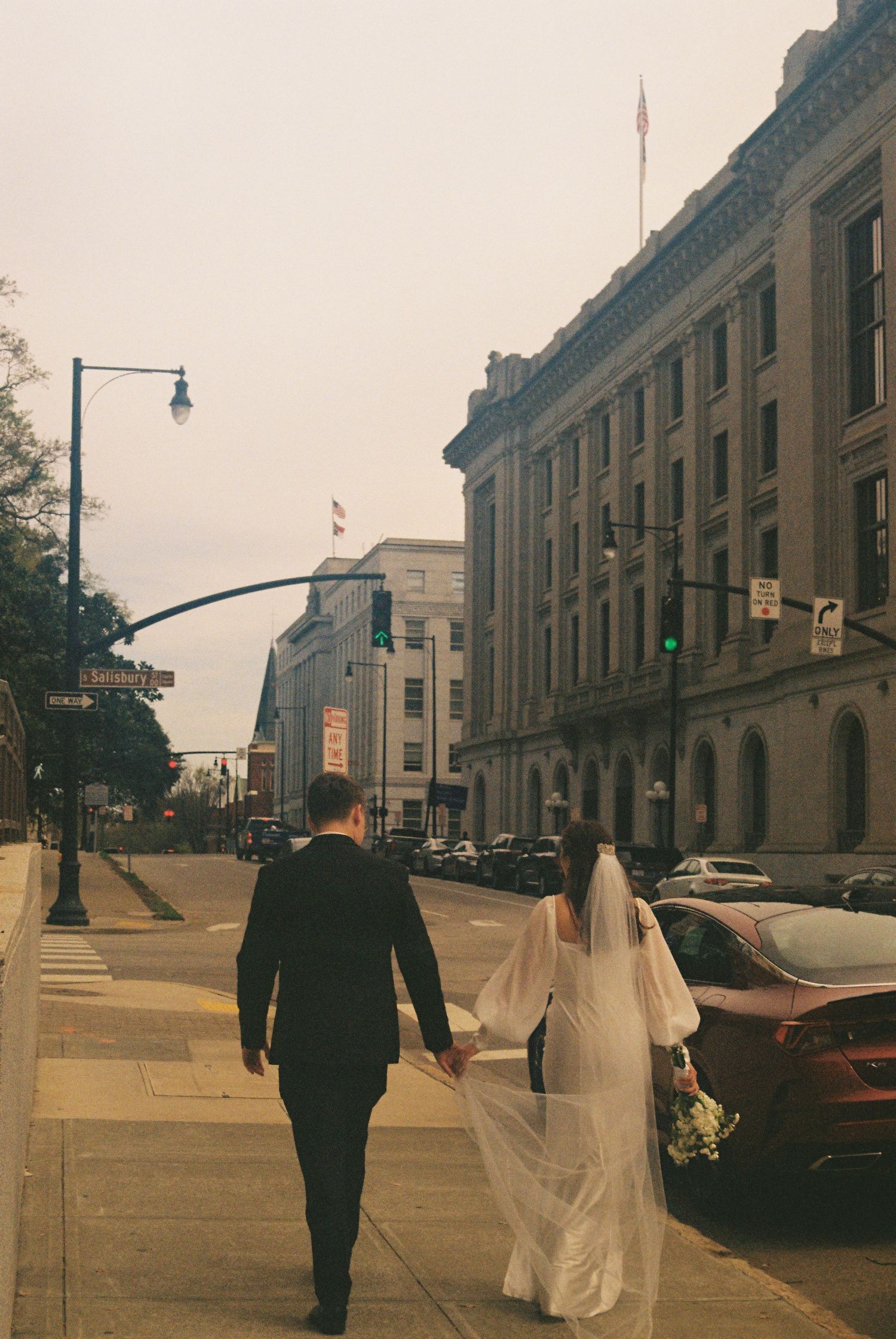 A couple walking together on a city street, with a bride wearing a long white dress.