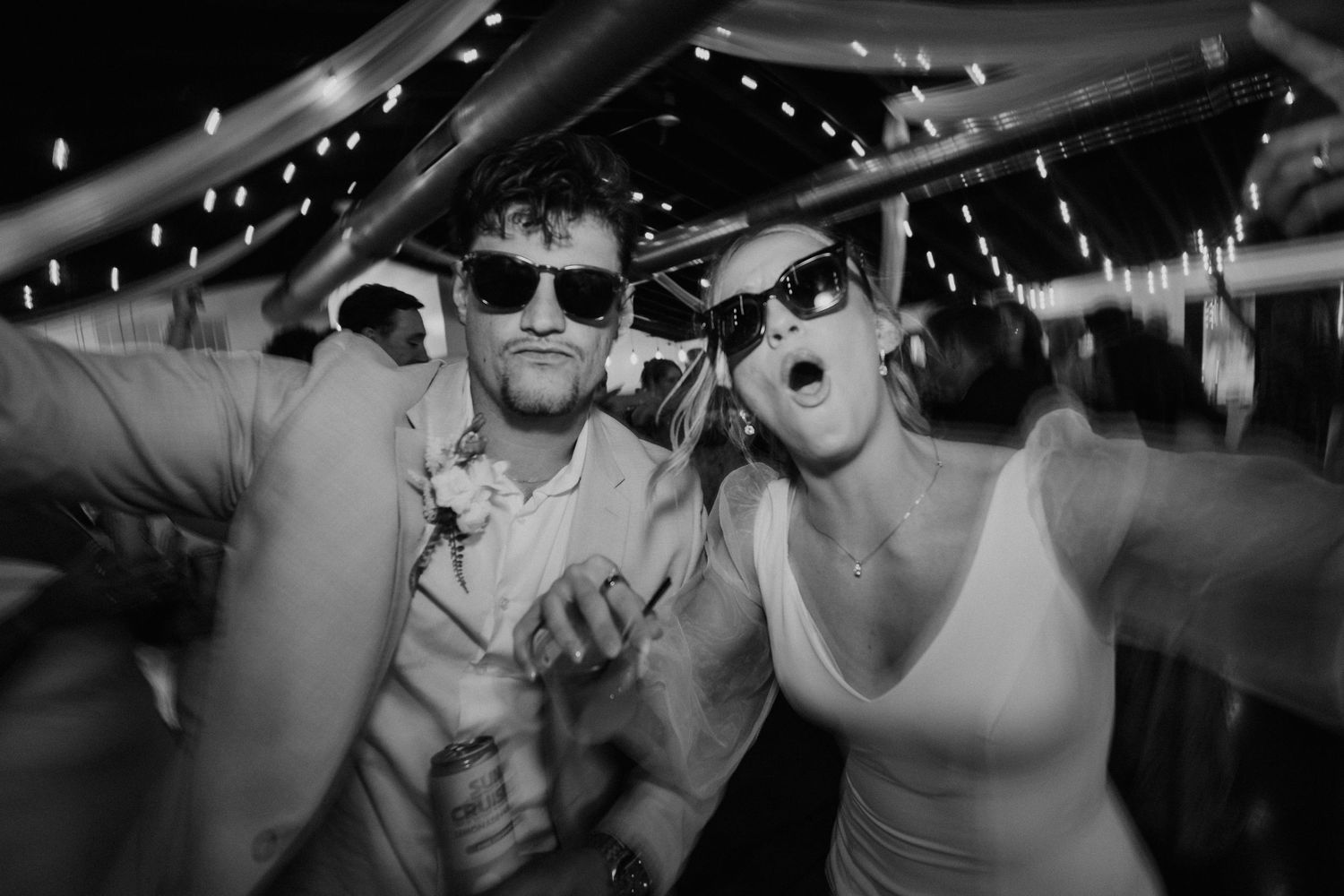 Black and white photo of two people wearing sunglasses dancing and celebrating at an outdoor evening party event.
