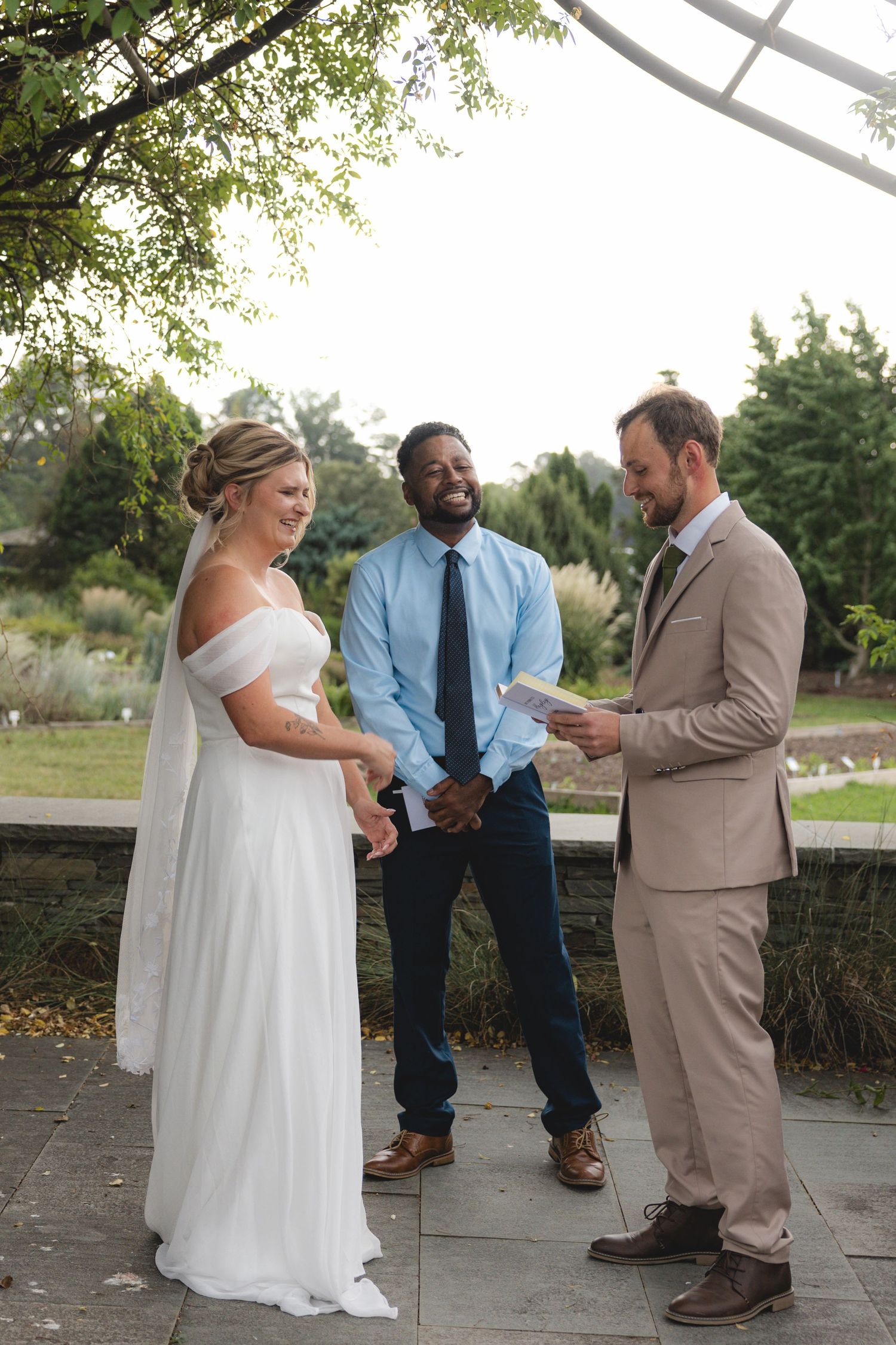 Bride and groom exchange vows outdoors with officiant in garden wedding ceremony.