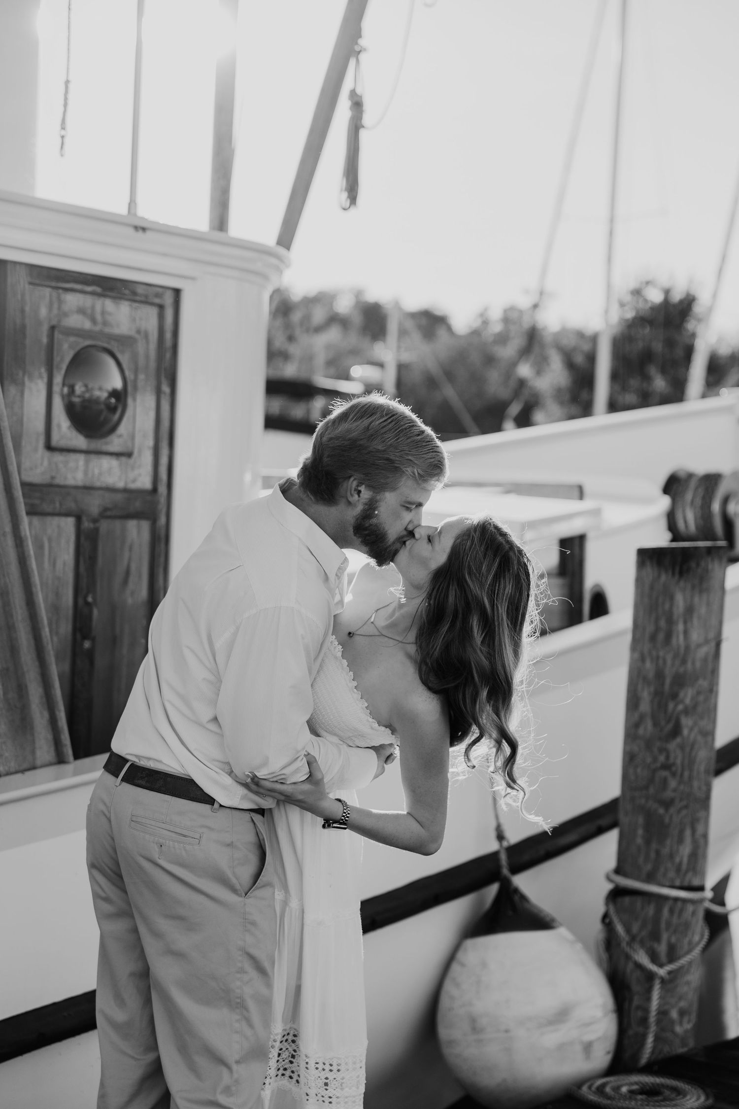 Couple sharing a romantic kiss on a boat dock in black and white engagement photo.