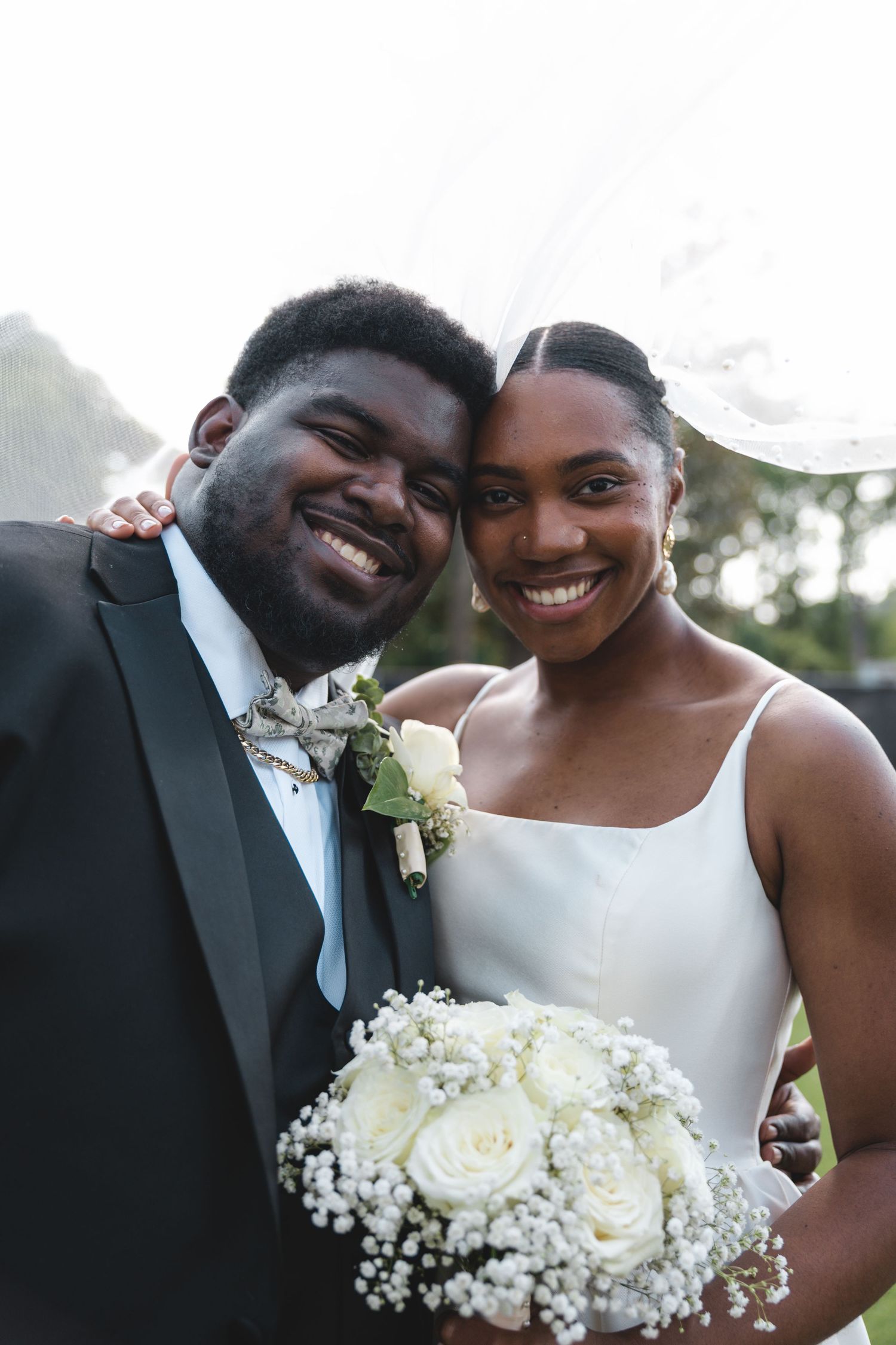 Smiling newlyweds pose together, bride holding white rose bouquet.
