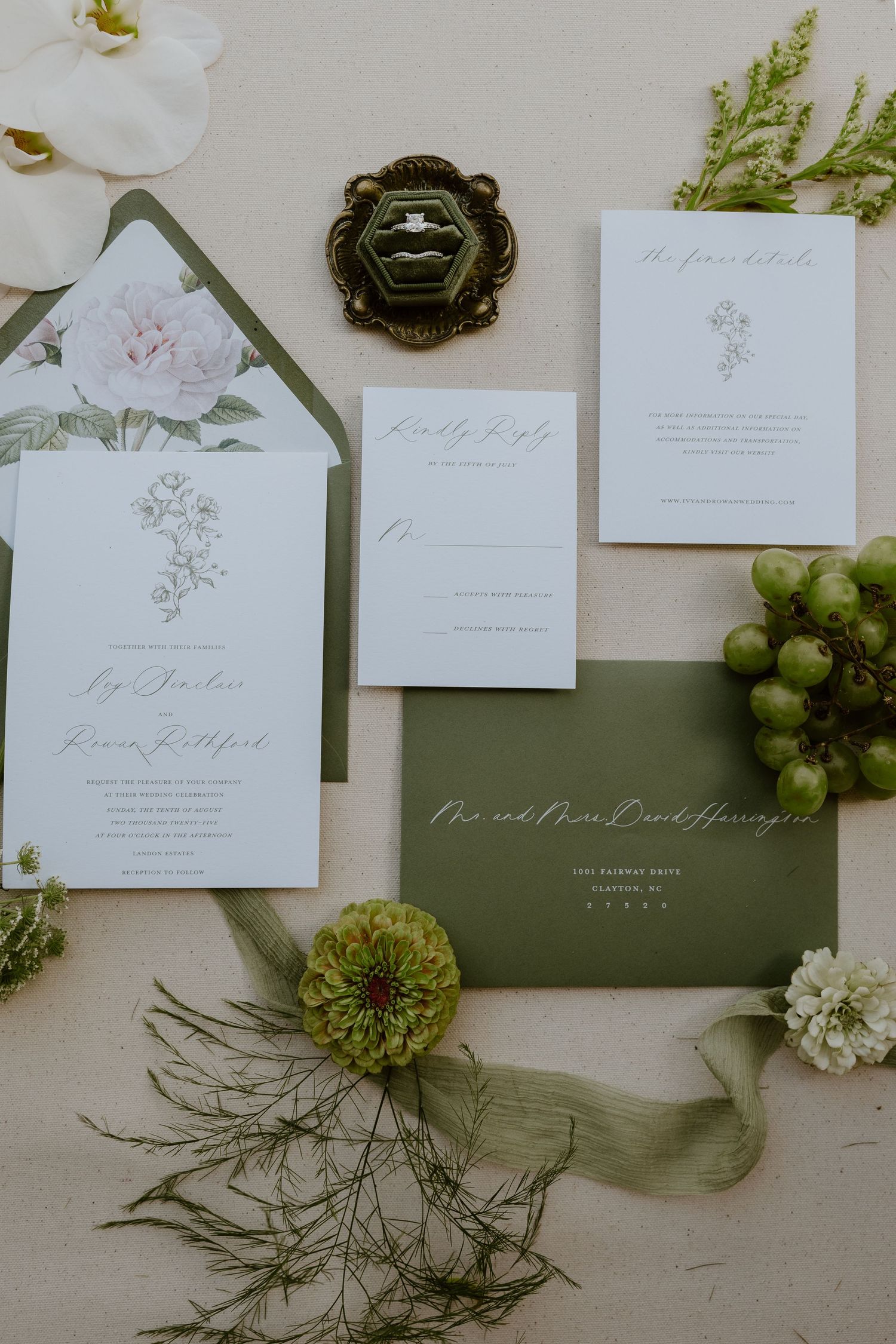 Elegant wedding invitation suite with floral details and green envelopes displayed with white flowers.