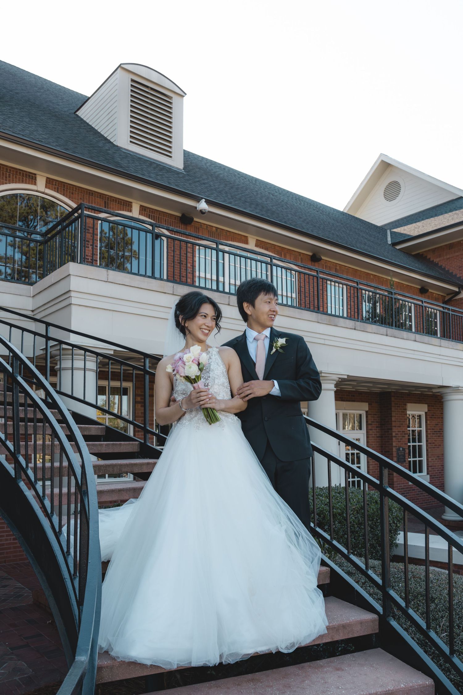 Bride and groom posing together on staircase outside brick wedding venue at dusk.