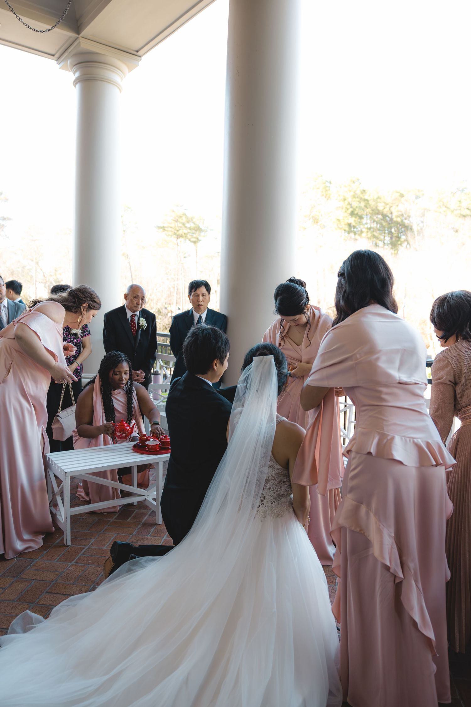 Bride and groom kneel during traditional Chinese tea ceremony with bridesmaids in pink.