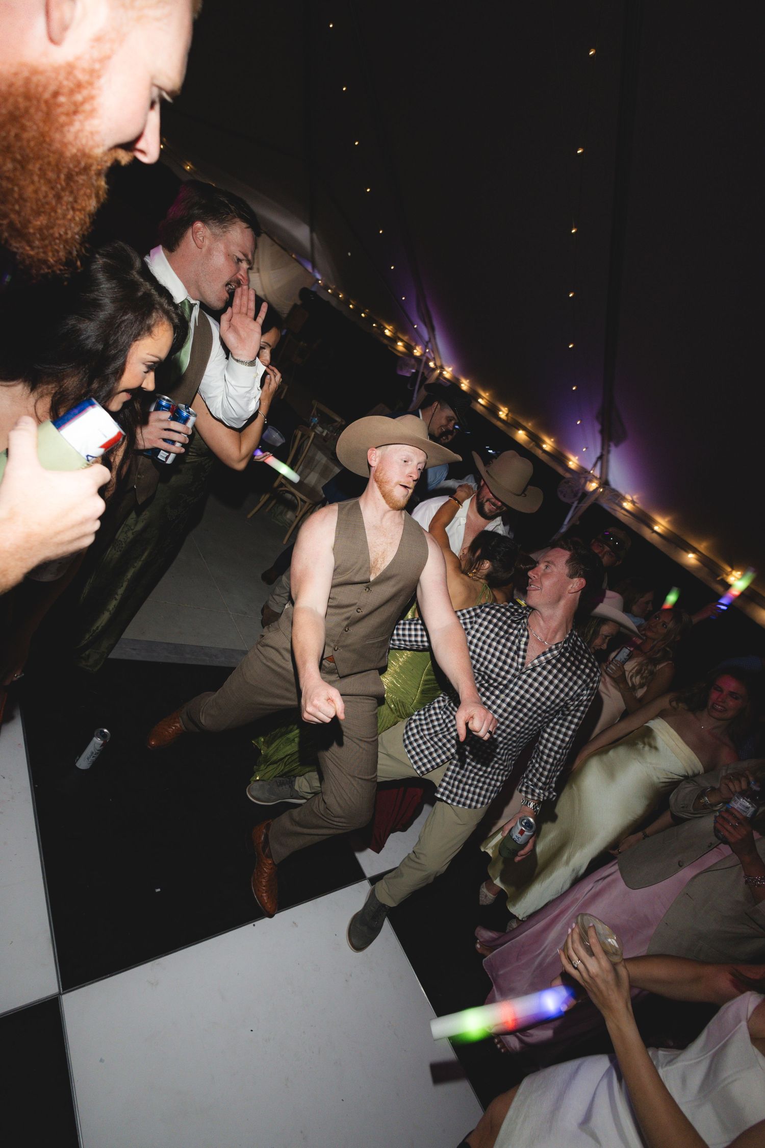 Energetic wedding guests jumping and dancing on a black and white checkered dance floor at a tented evening reception.
