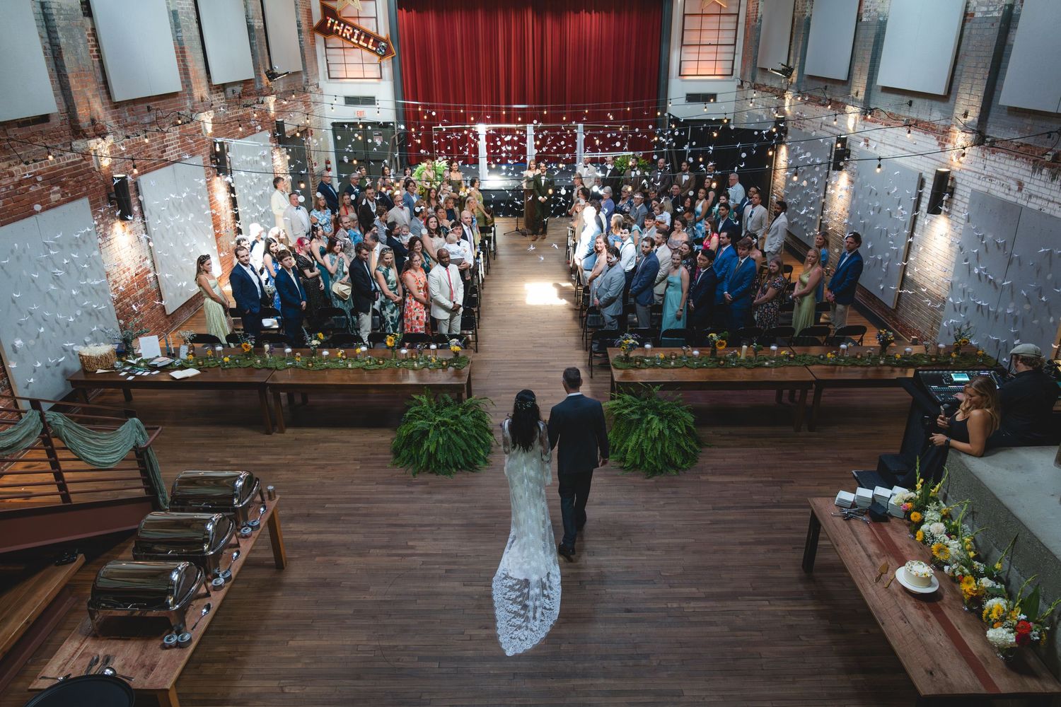 Aerial view of a bride and groom walking down the aisle at an elegant indoor wedding ceremony with guests seated.