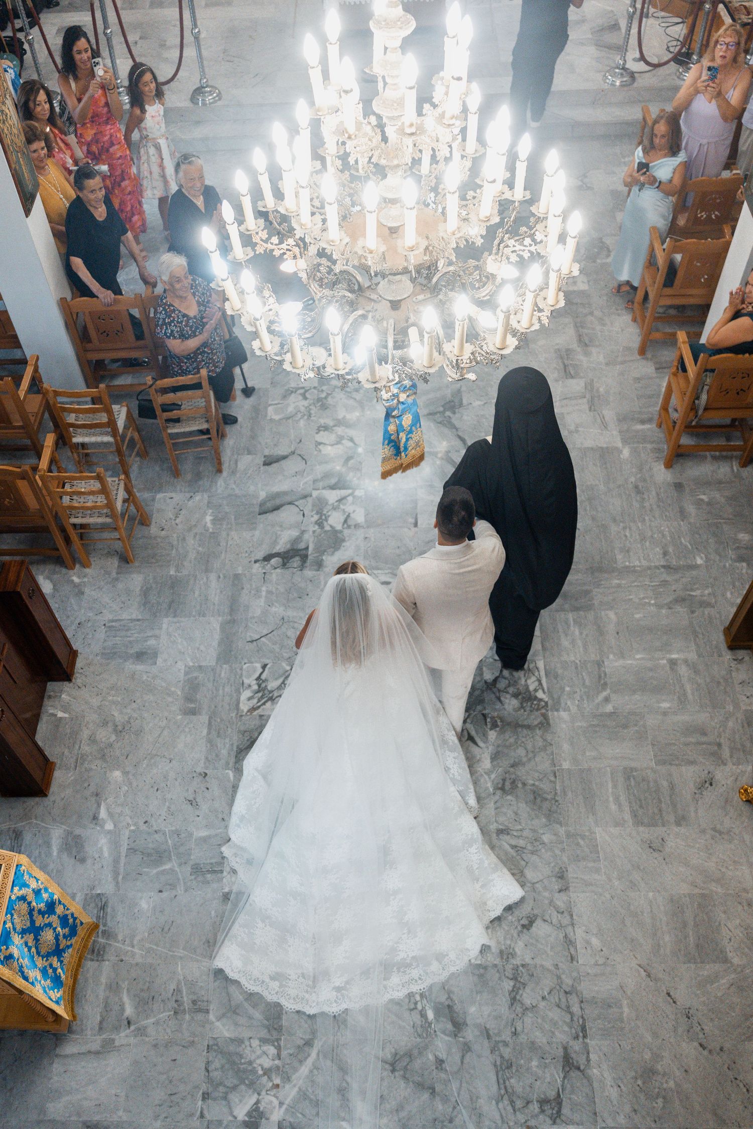 Aerial view of a bride in white gown walking down church aisle with priest during wedding ceremony.