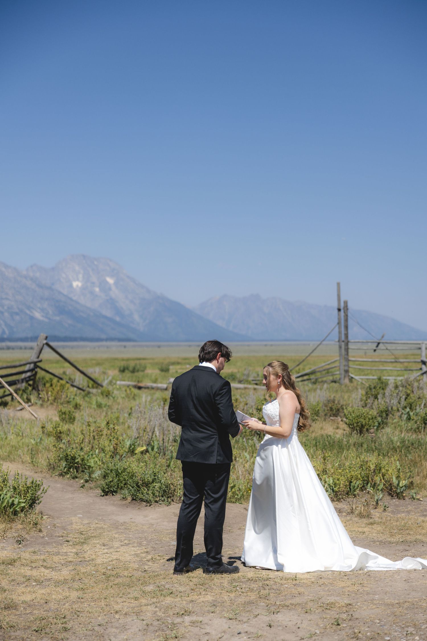 Bride and groom exchange vows outdoors with Grand Teton mountains backdrop on a sunny day.