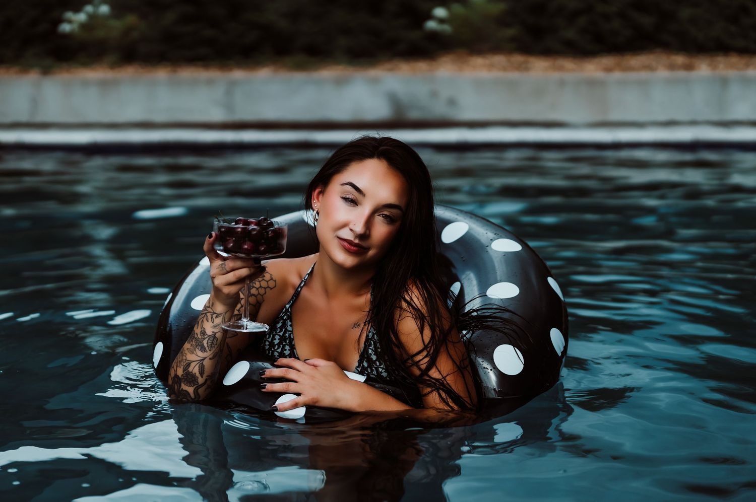 Woman relaxing in polka dot pool float holding a drink in an outdoor swimming pool.