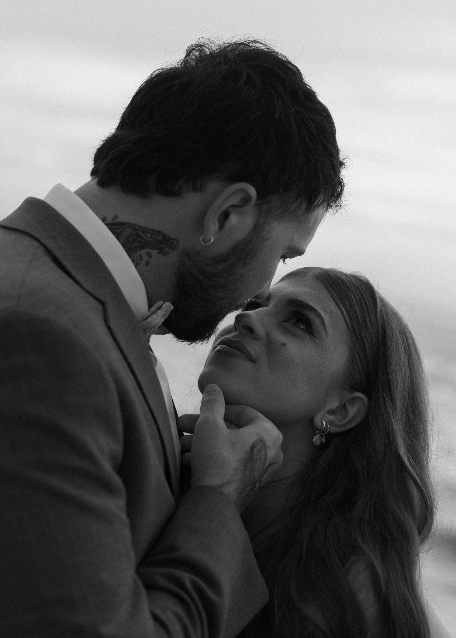 Black and white romantic photo of a bearded man in a suit gently lifting a woman's chin as they share an intimate moment.