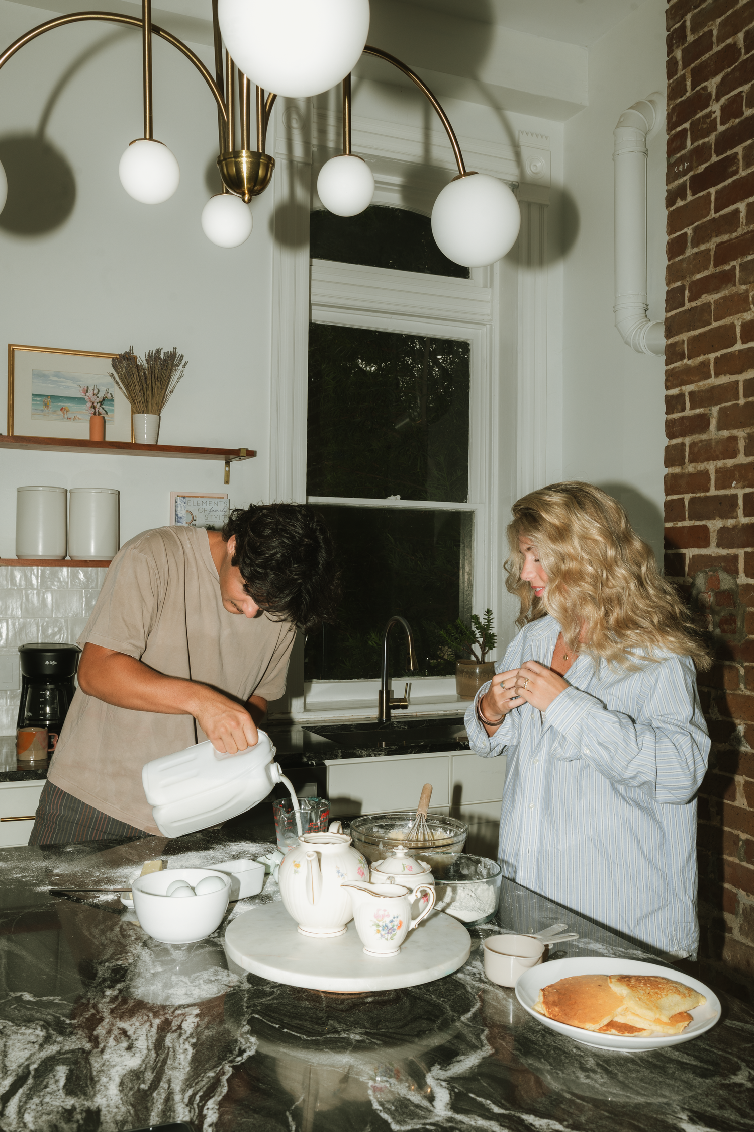 Couple preparing tea at a marble kitchen island under modern globe pendant lights in a bright white kitchen.