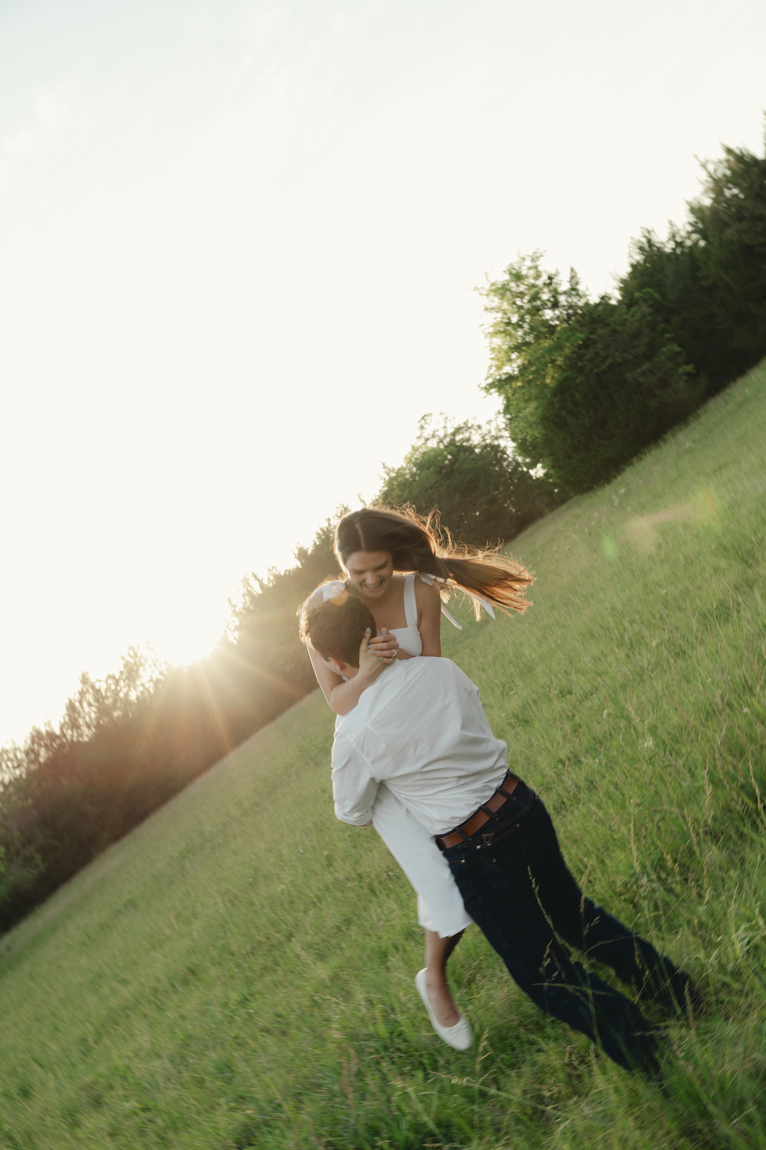 Couple sharing a romantic piggyback ride in a sunlit green field at golden hour.
