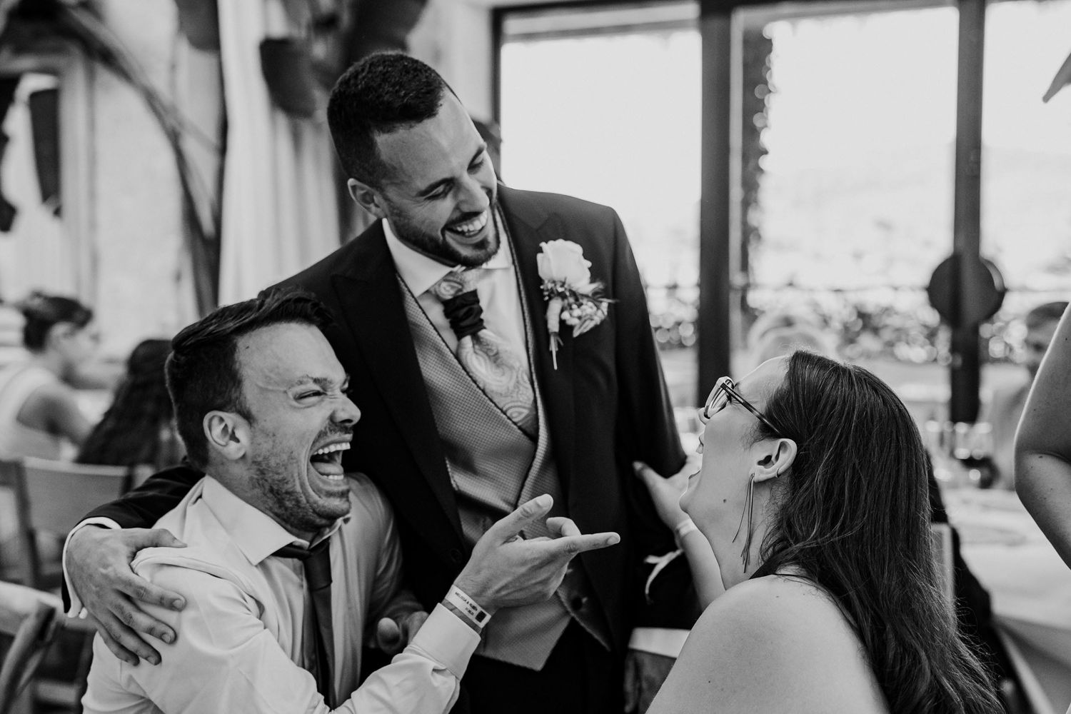 Groom laughing with wedding guests during lively reception celebration.