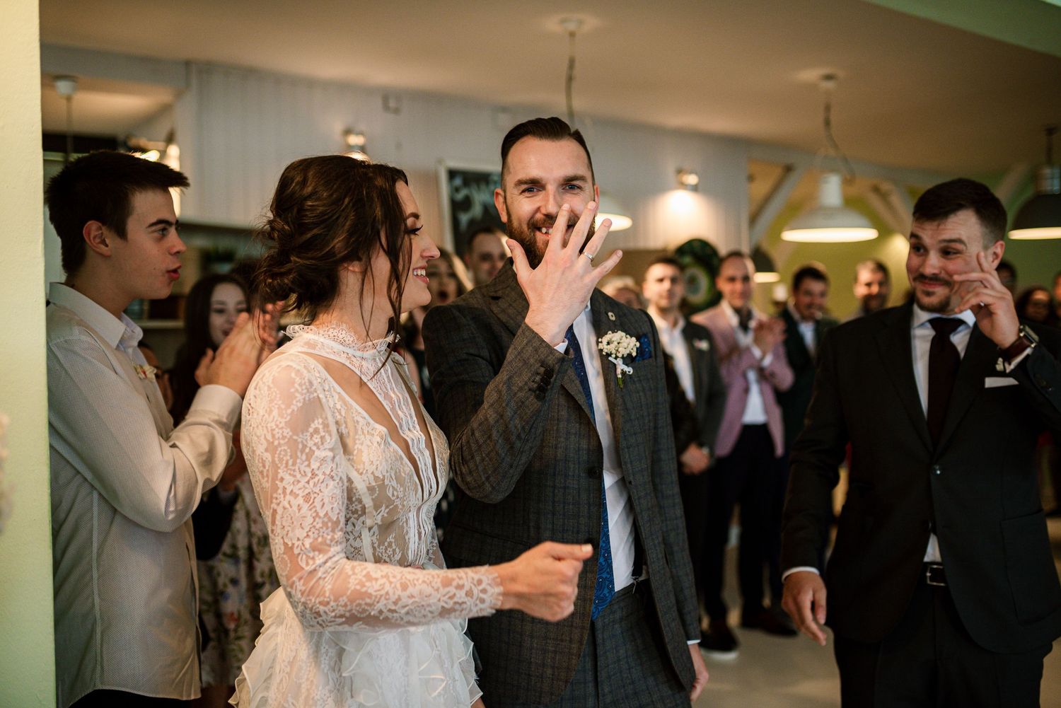 Groom reacts with surprise and joy as bride holds his hand during wedding reception entrance.