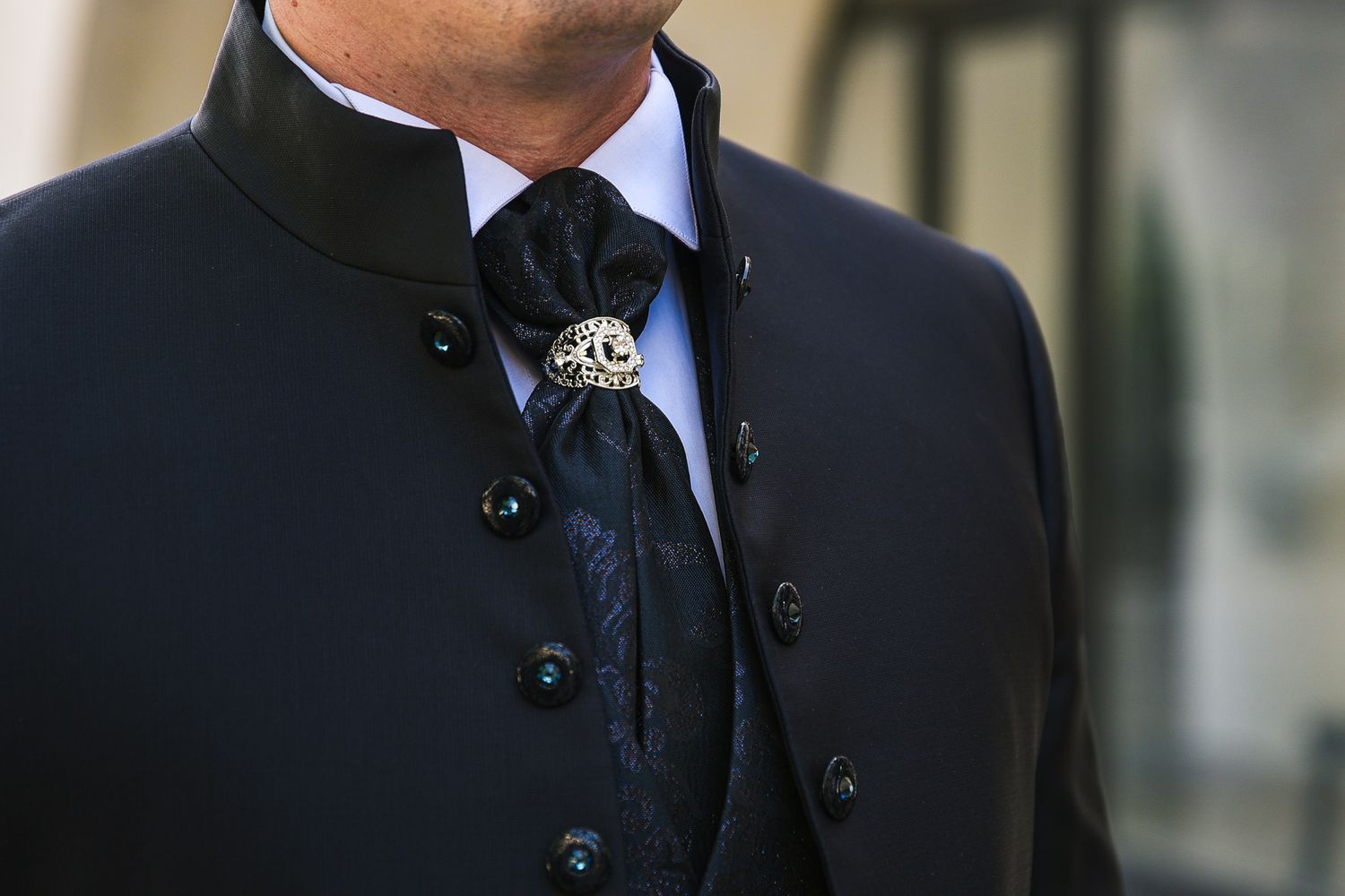 Close-up of groom in black formal coat with decorative bolo tie at wedding.
