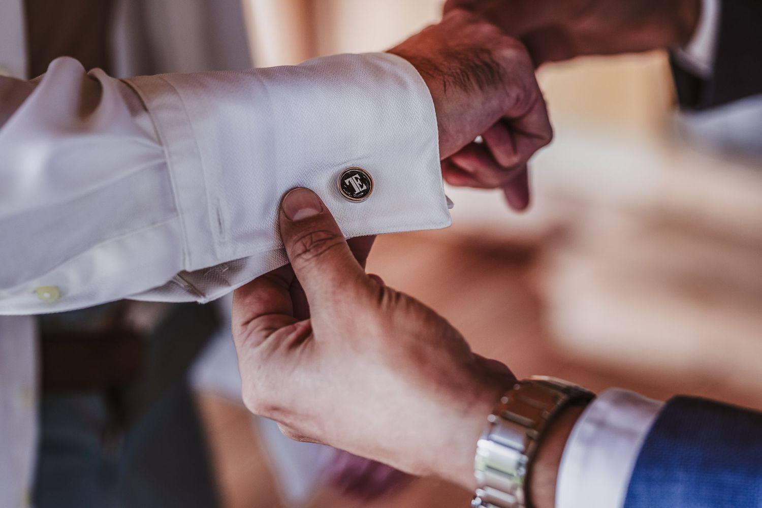 Close-up of groom's cufflink being fastened on white dress shirt sleeve.