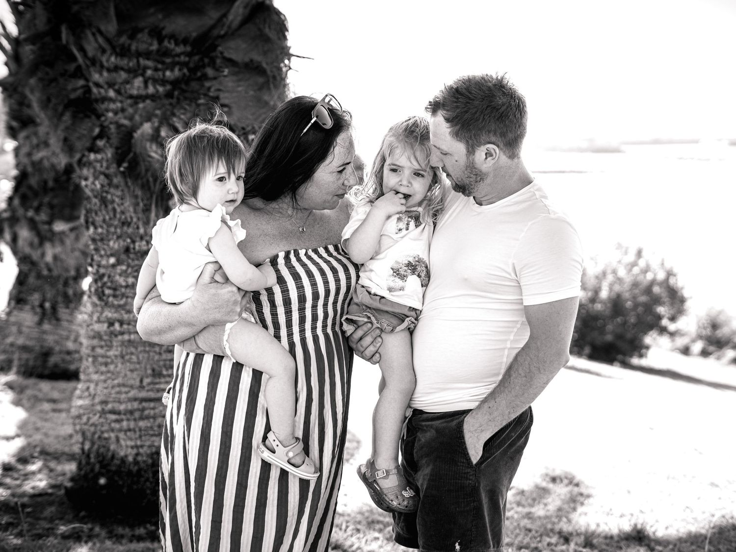 Black and white photo of loving family of four sharing a joyful moment by a palm tree.